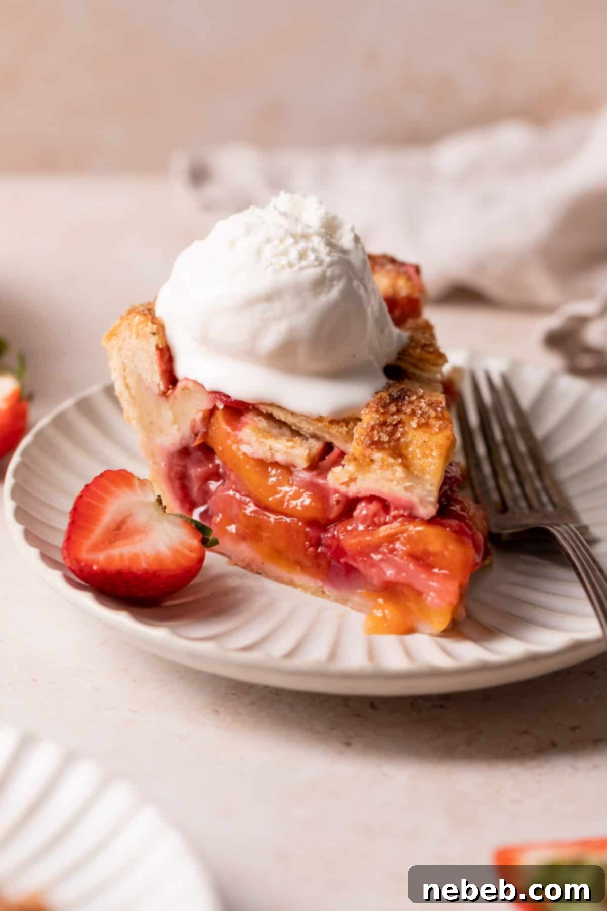 A perfectly sliced piece of strawberry peach pie with a melting scoop of vanilla ice cream on top, presented on a white plate.