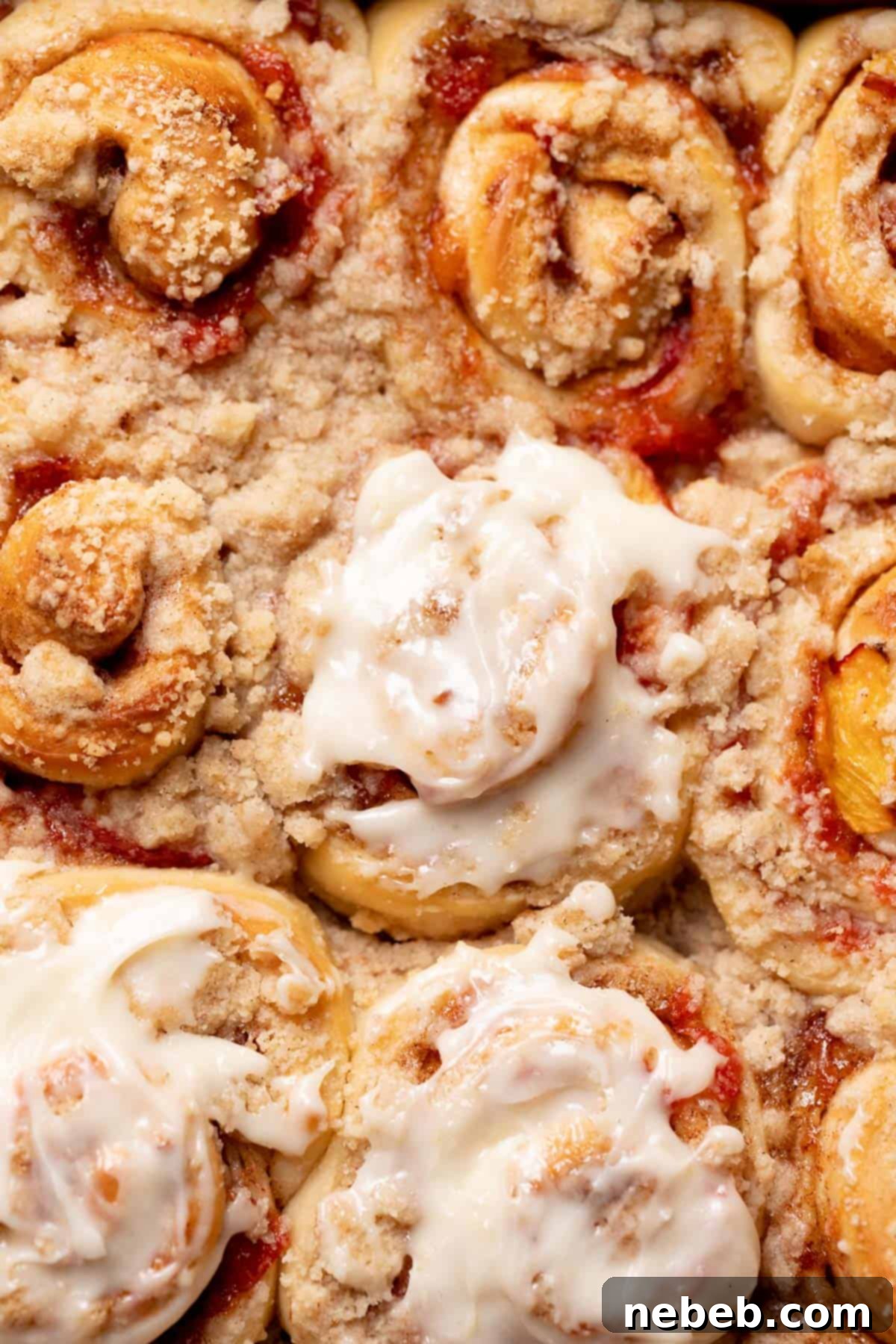 Close-up of baked peach cobbler cinnamon rolls with cream cheese icing, highlighting the crumb topping and peach filling.