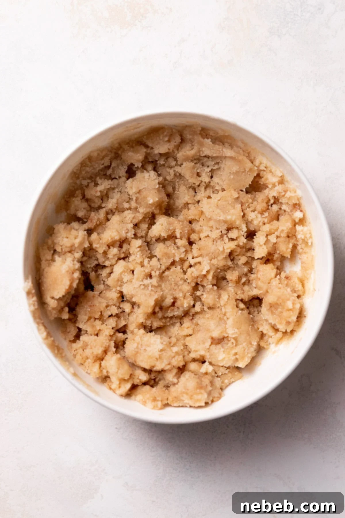 A bowl containing cinnamon crumb topping, ready to be sprinkled on the rolls.