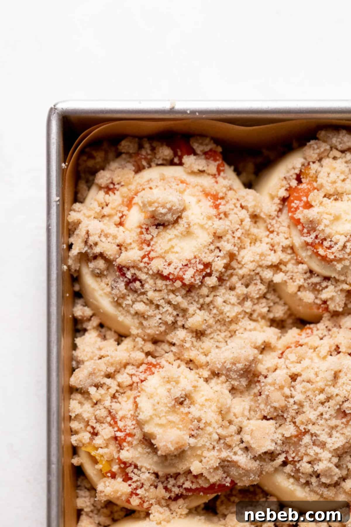 Peach cobbler cinnamon rolls with crumb topping sprinkled over them in a baking pan, just before going into the oven.