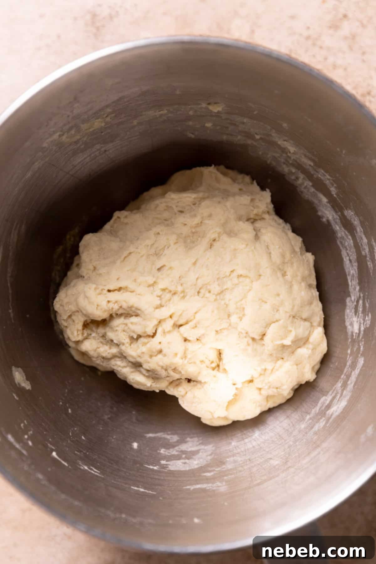 A mixing bowl with a rough, shaggy dough ball beginning to form.
