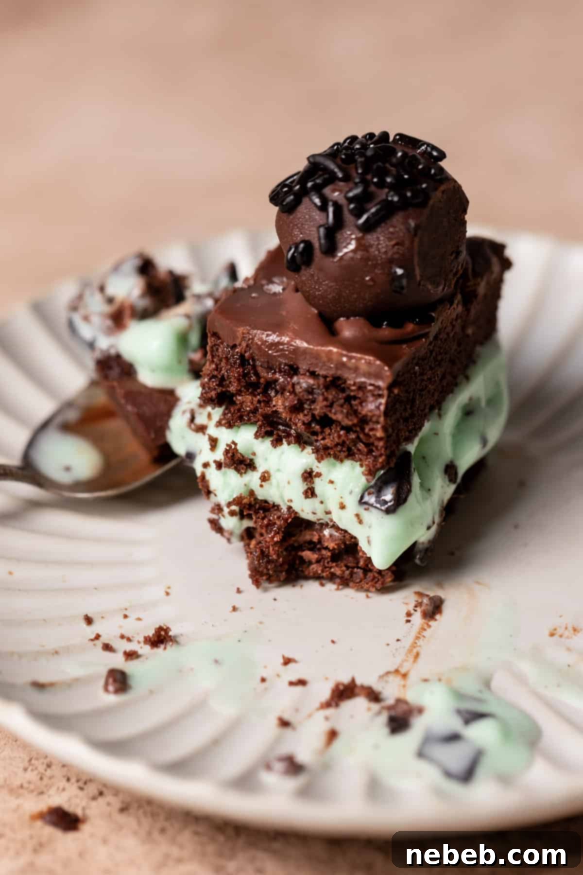 A perfectly portioned slice of mint chocolate chip ice cream cake on a white plate, with a fork ready to enjoy.