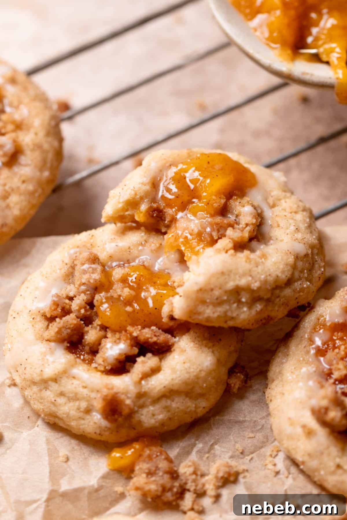 A perfectly baked peach cobbler cookie with a bite taken out, showcasing the jammy peach filling, crumb topping, and glaze.