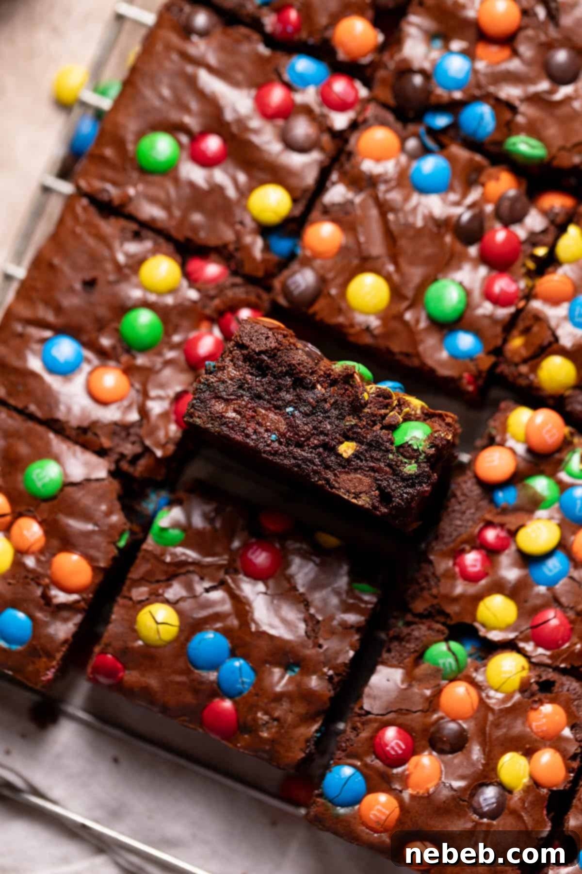 Fudgy M&M brownies on a wire rack with one on its side to show the rich, gooey texture.