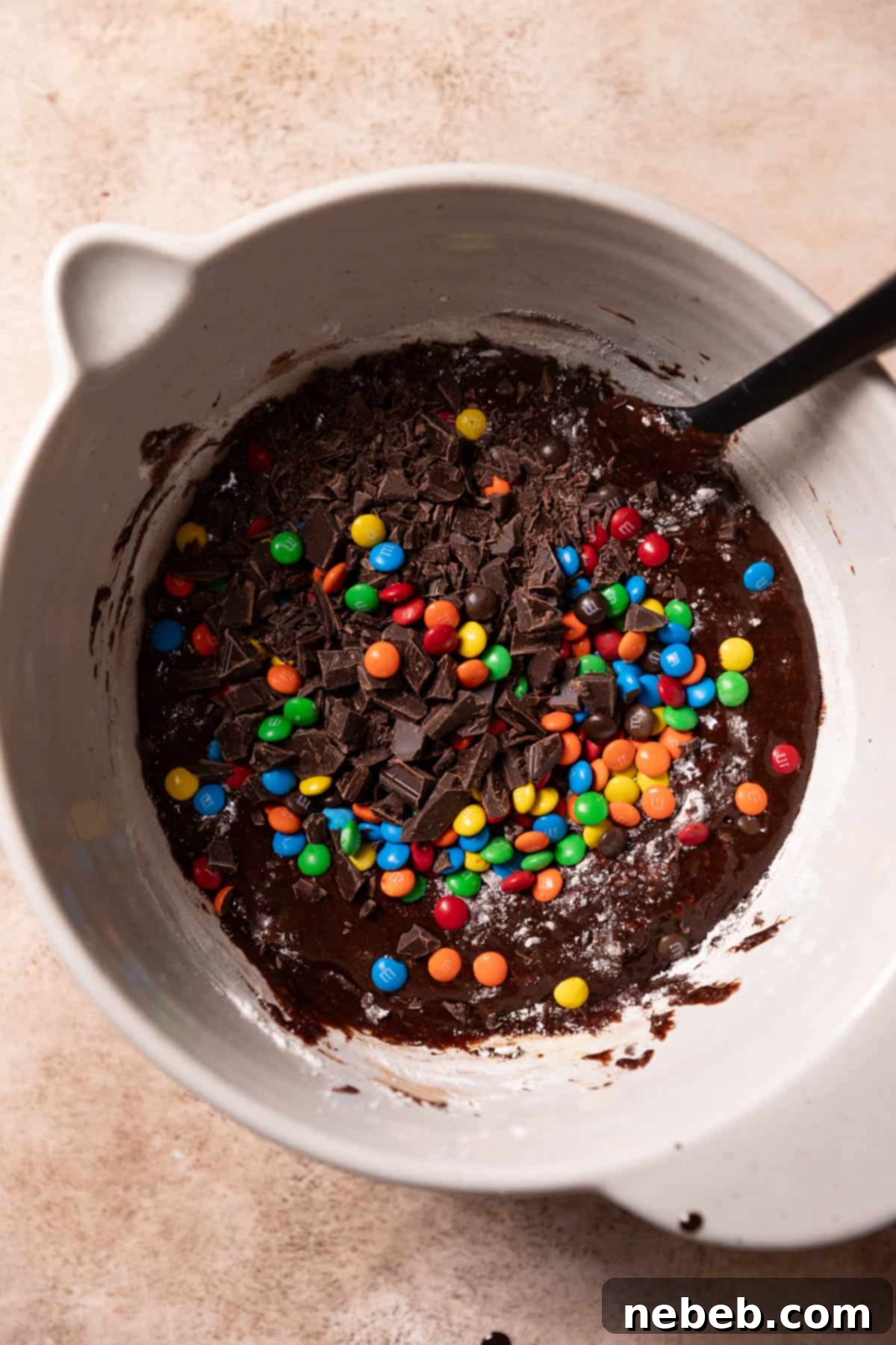 Brownie batter in a bowl with M&Ms and chocolate chunks on top, ready for final folding.