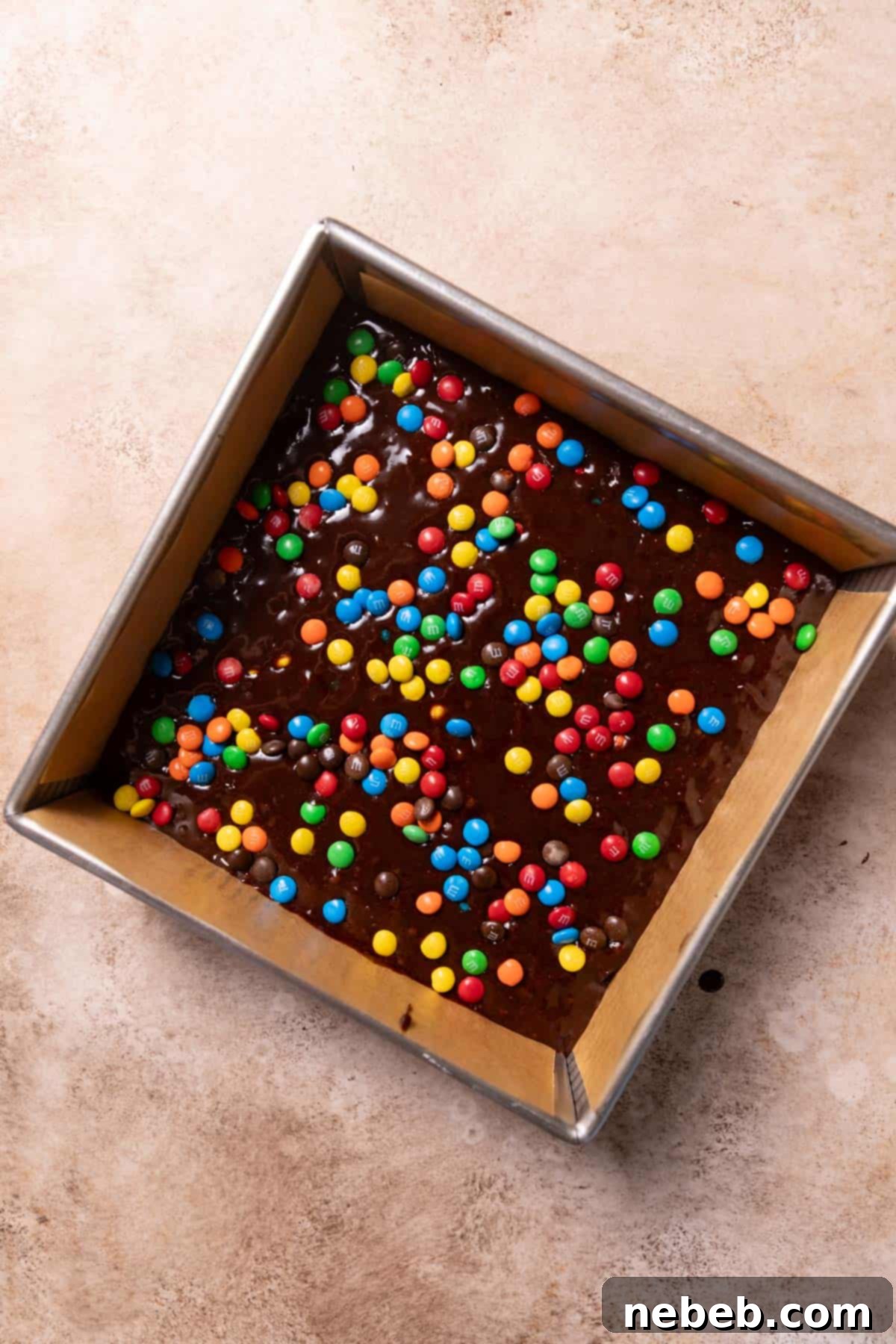 M&M brownie batter in a prepared pan with extra M&M candies sprinkled on top before baking.