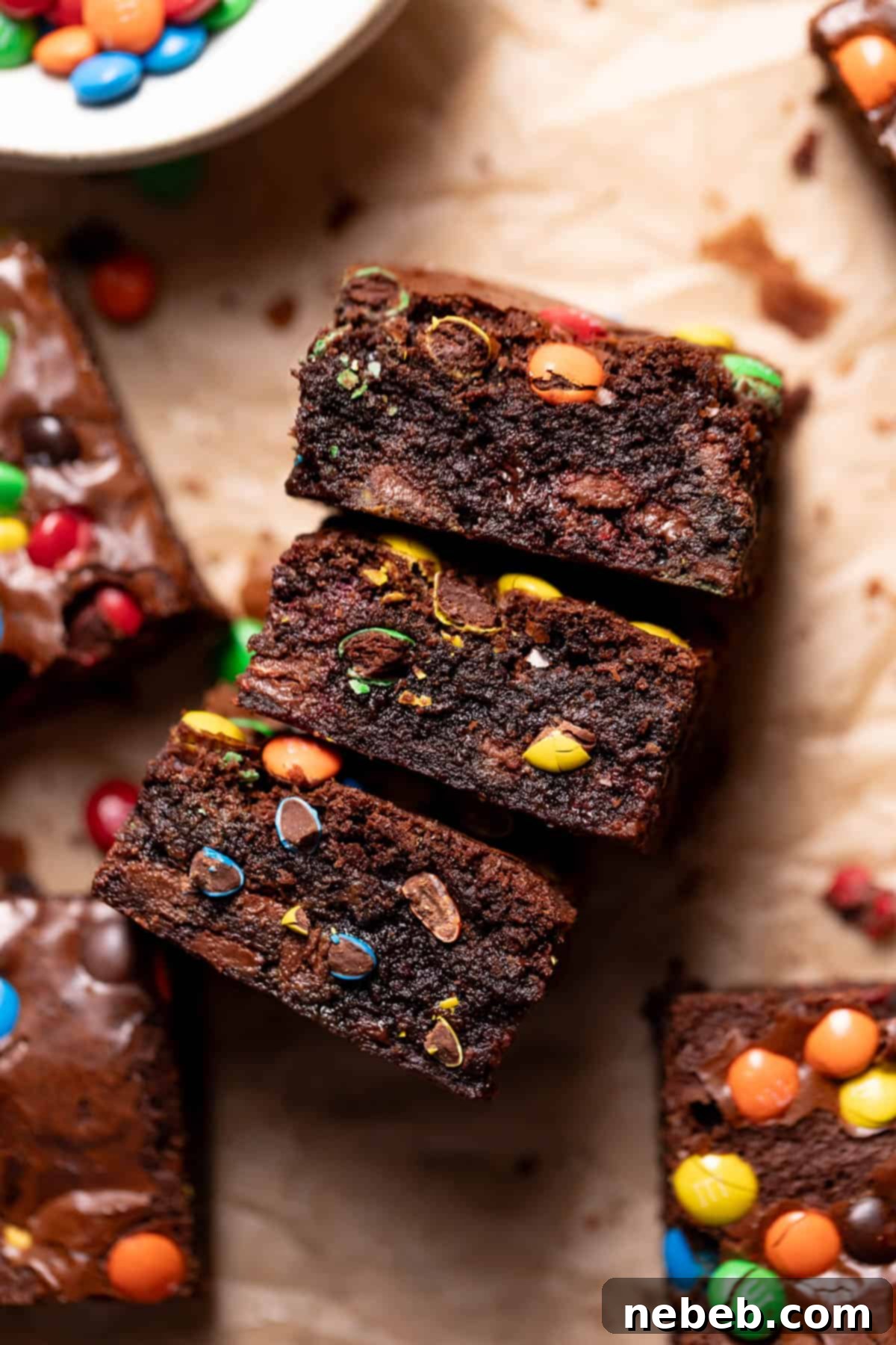 Three fudgy M&M brownies with colorful M&Ms on parchment paper, ready to be enjoyed.