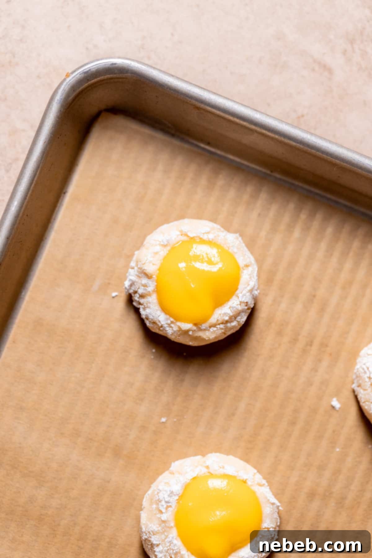 A cookie dough ball on a baking tray with a clear indentation in the center, filled with bright mango curd, ready for chilling.