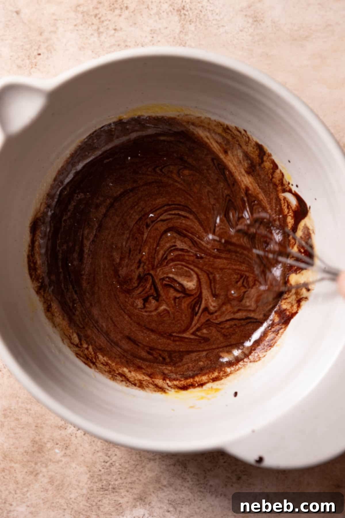 Combining the melted chocolate mixture into the whisked egg mixture for brownie batter.