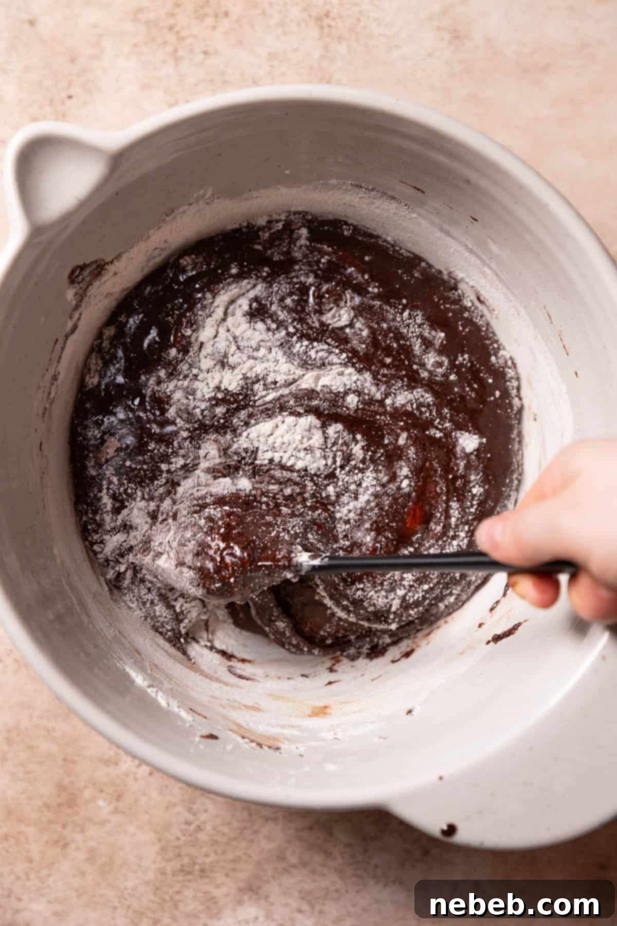 Gently folding dry ingredients (flour, espresso, salt) into the brownie batter with a rubber spatula.
