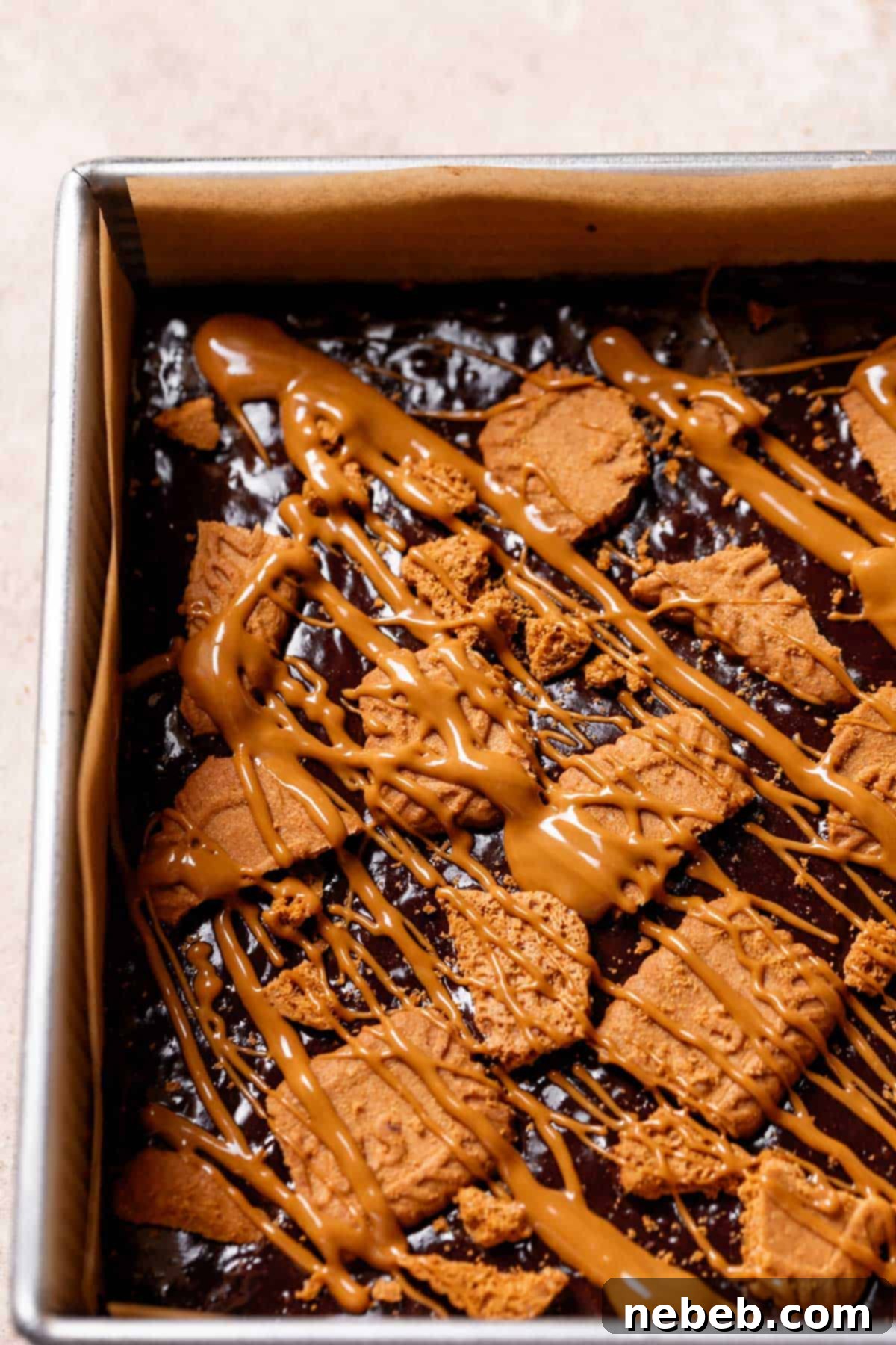 Unbaked Biscoff brownies topped with crushed Biscoff cookies and drizzled cookie butter, ready for the oven.