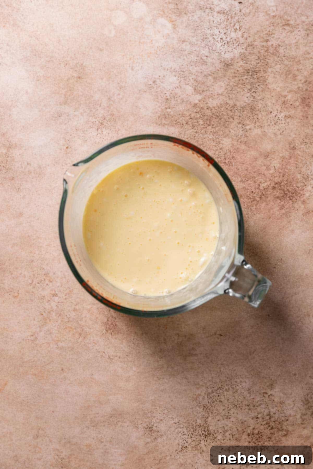 A glass measuring cup with whisked eggs and cream.