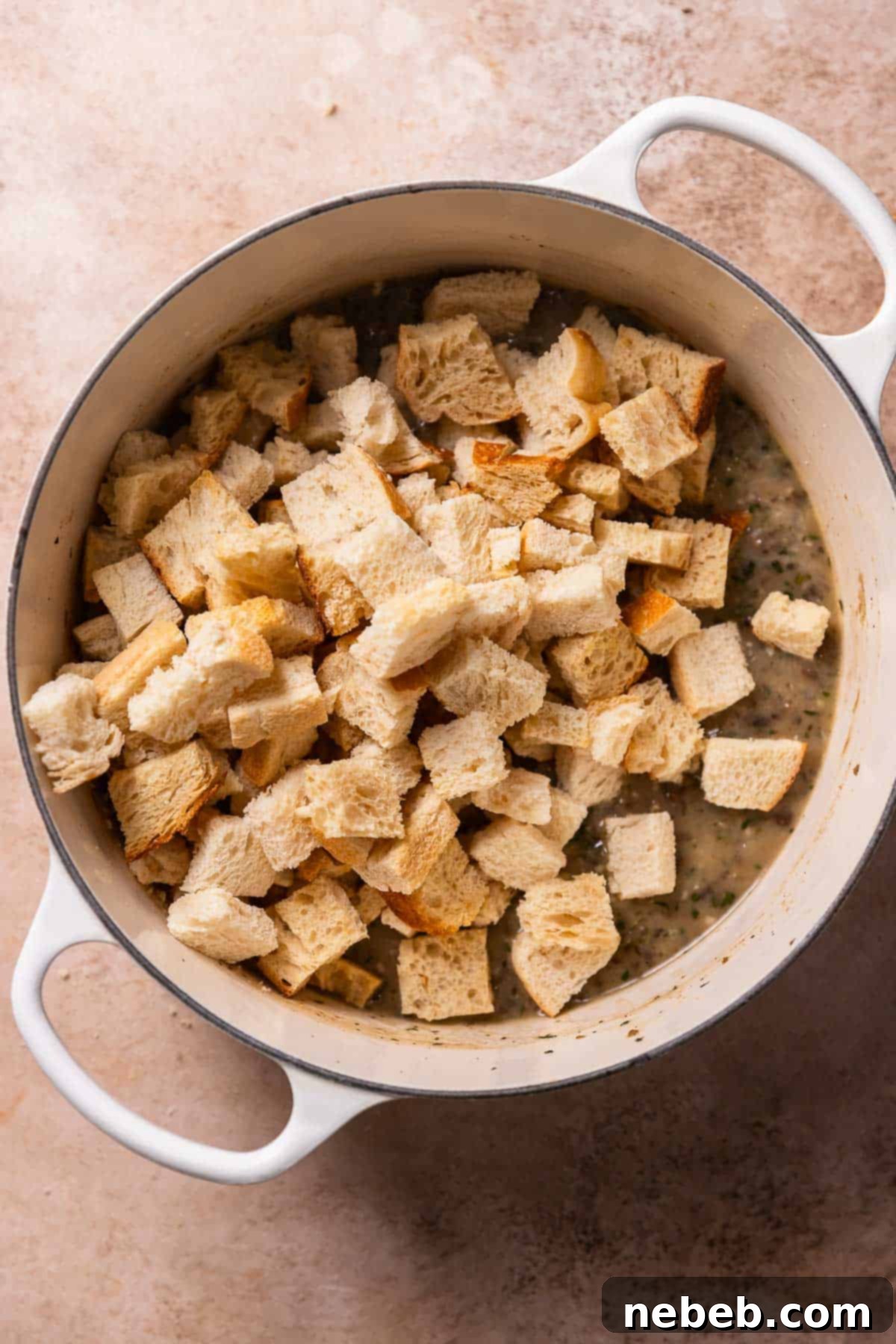 A dutch oven with the sauce on the bottom and cubed pieces of bread on top.