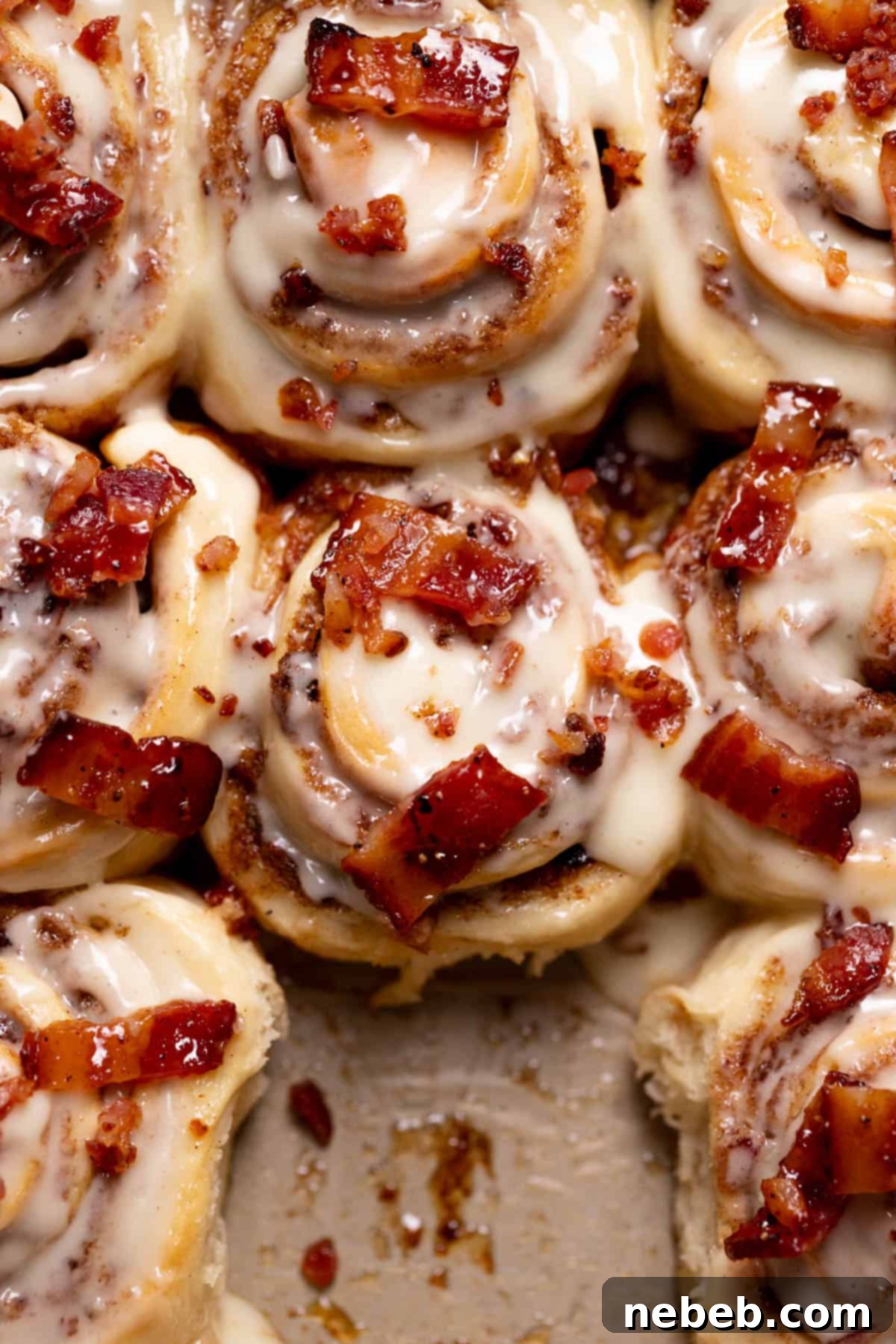 bacon cinnamon rolls with maple frosting and candied bacon in a baking pan.
