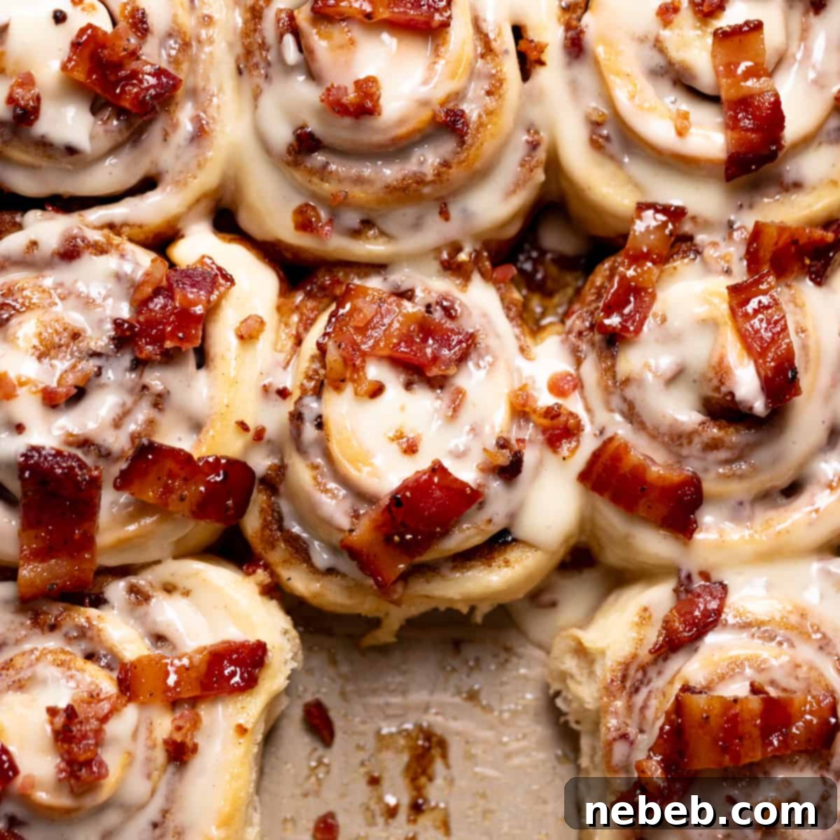 cinnamon rolls in a pan with maple frosting and candied bacon on top.