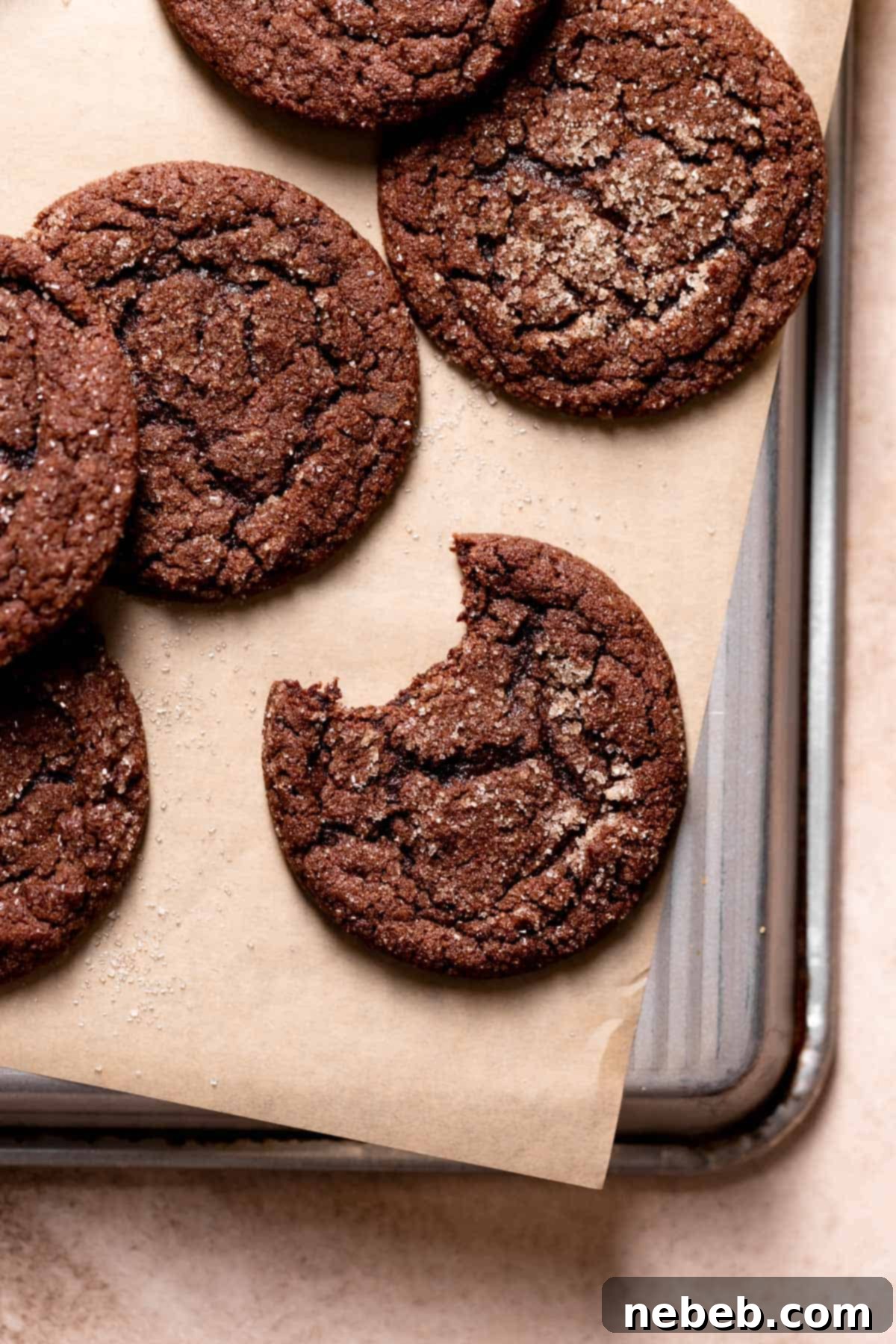 A perfectly baked chocolate snickerdoodle cookie with a bite taken out of it, showing its soft, chewy interior, resting on a parchment-lined tray.