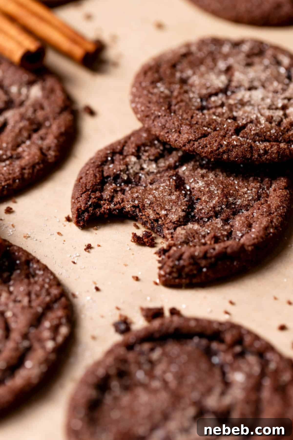 A close-up of a chewy chocolate snickerdoodle cookie with a bite taken out, showing its soft texture, on parchment paper.