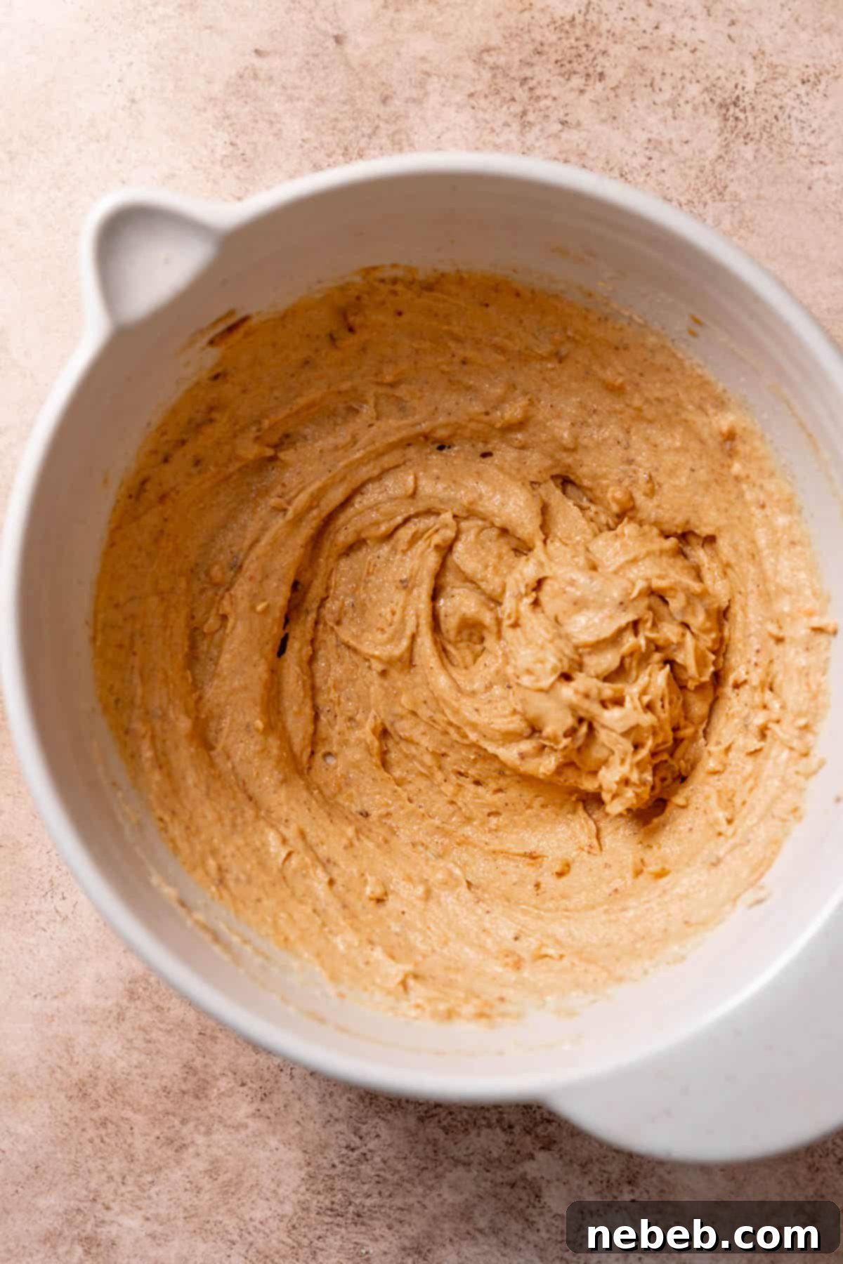 A mixing bowl with the perfectly blended wet ingredients, including pumpkin puree, egg yolks, and vanilla, stirred into the creamed butter and sugar.