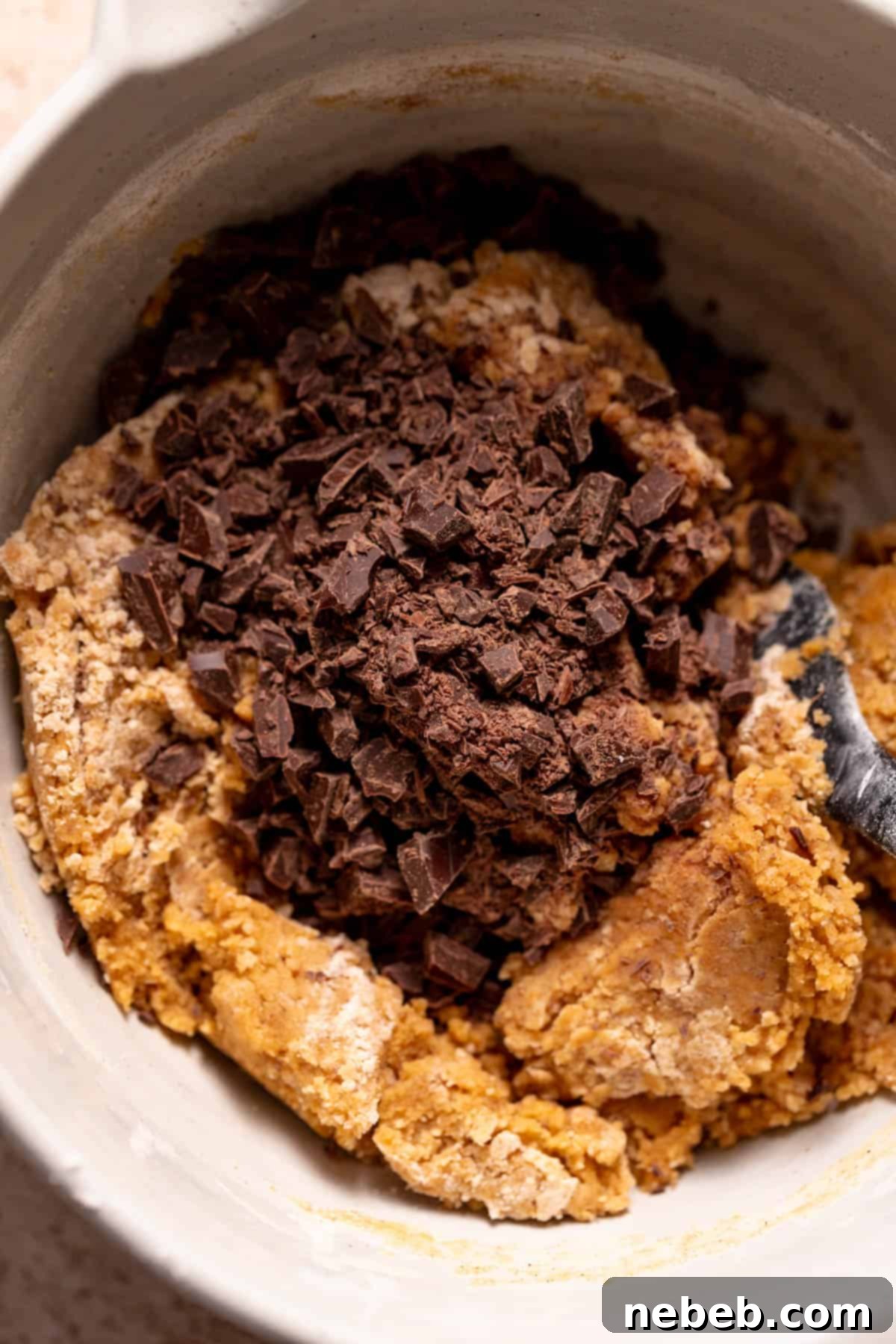 A mixing bowl filled with rich pumpkin cookie dough, with a generous scattering of chocolate chips layered on top, ready for the final fold.