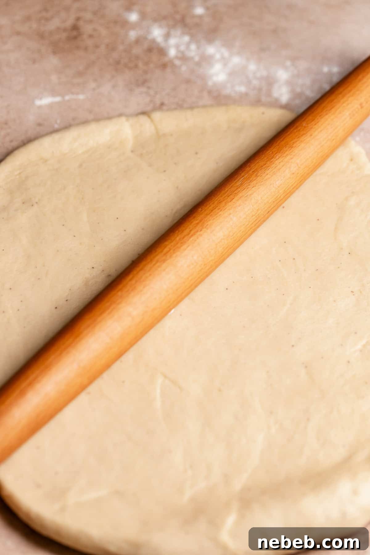 A rolling pin rolling out the apple bun dough.