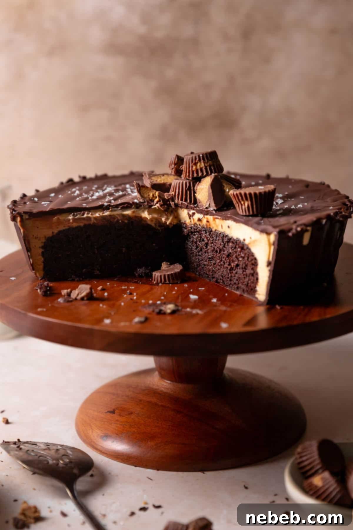 A stunning Reese's peanut butter cake on a wooden cake stand with some slices missing, revealing its decadent layers of chocolate cake and peanut butter filling.