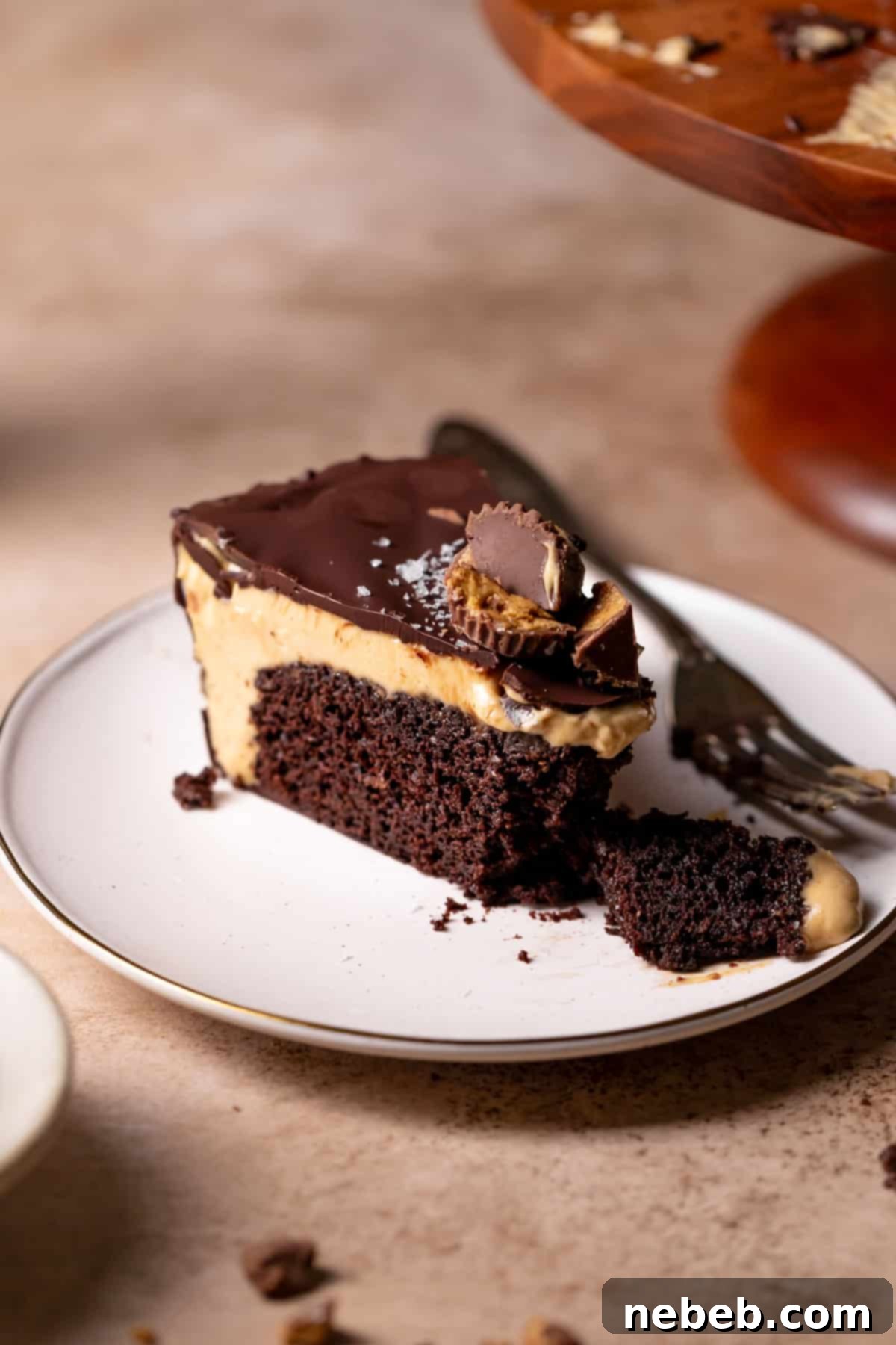A perfectly sliced Reese's cake on a white plate, garnished with miniature peanut butter cups and flaky sea salt, ready to be enjoyed.
