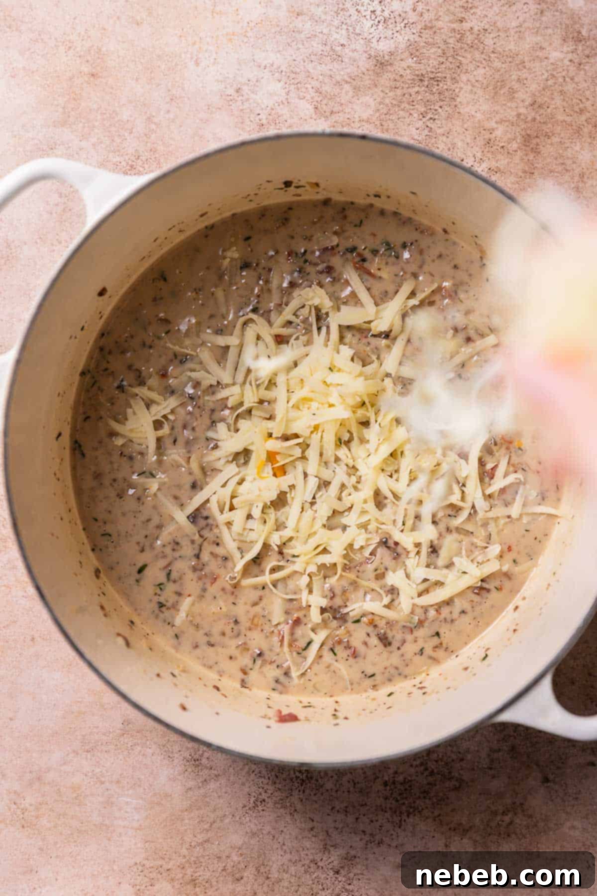 A hand sprinkling shredded cheese into the creamy gravy for the cheesy green bean casserole.