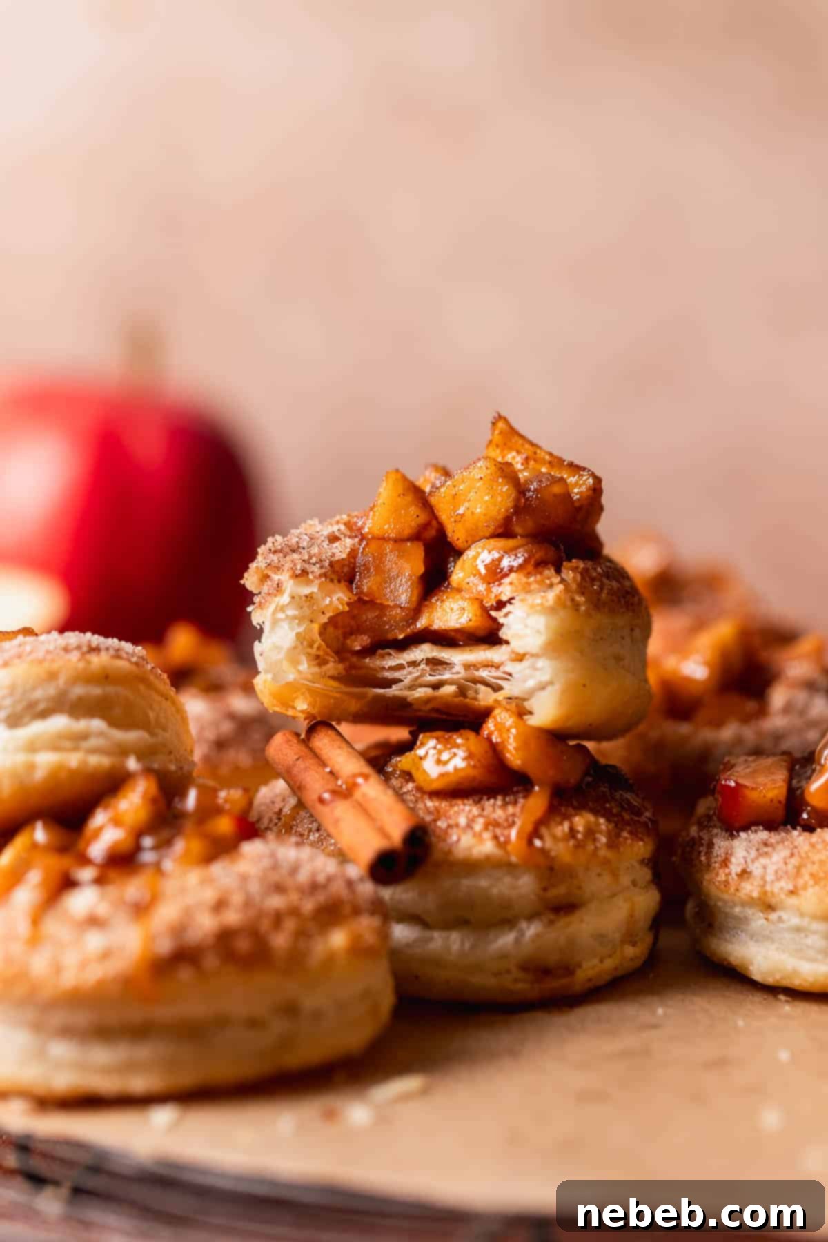 Two apple cookies stacked on top of each other with the top one missing a bite to show the flaky pastry layers.