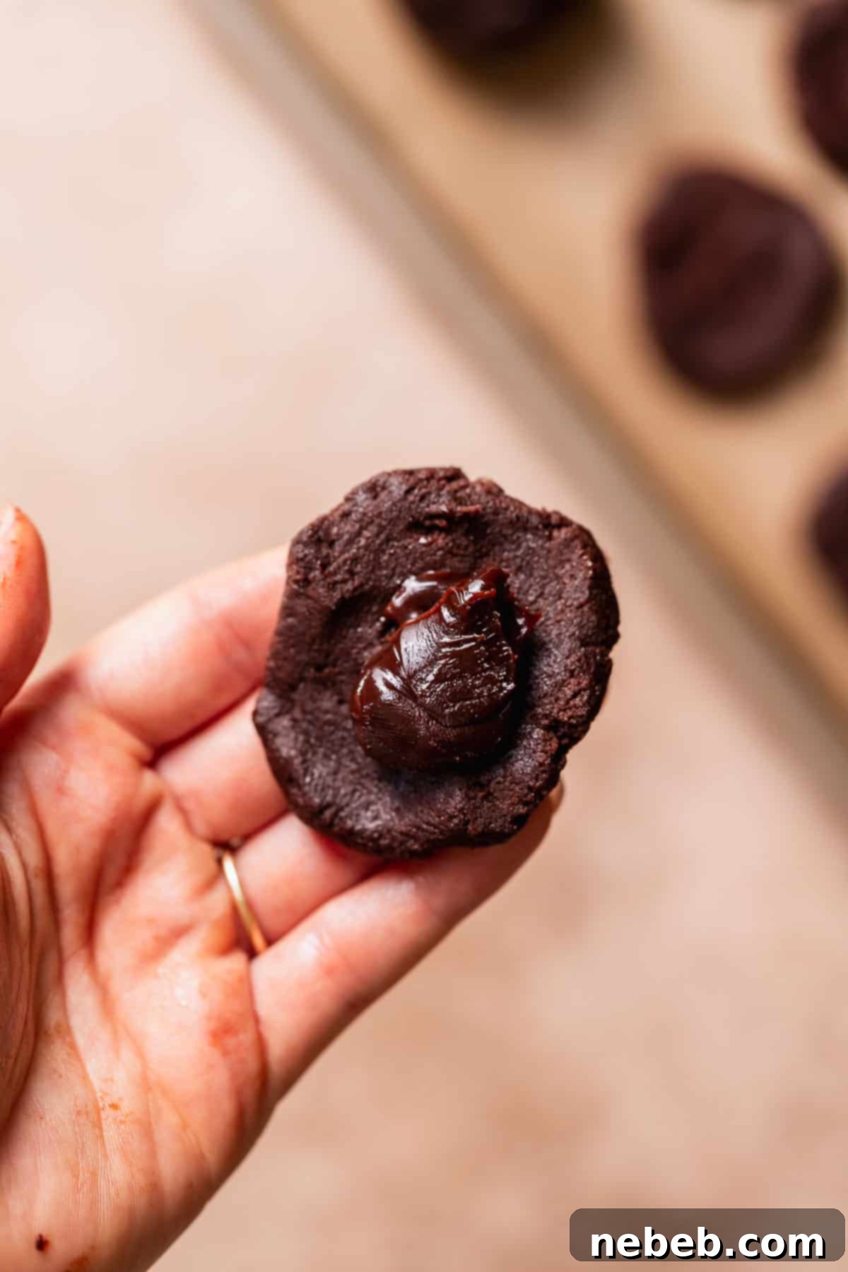A hand holding a cookie dough round with fudge filling in the center.