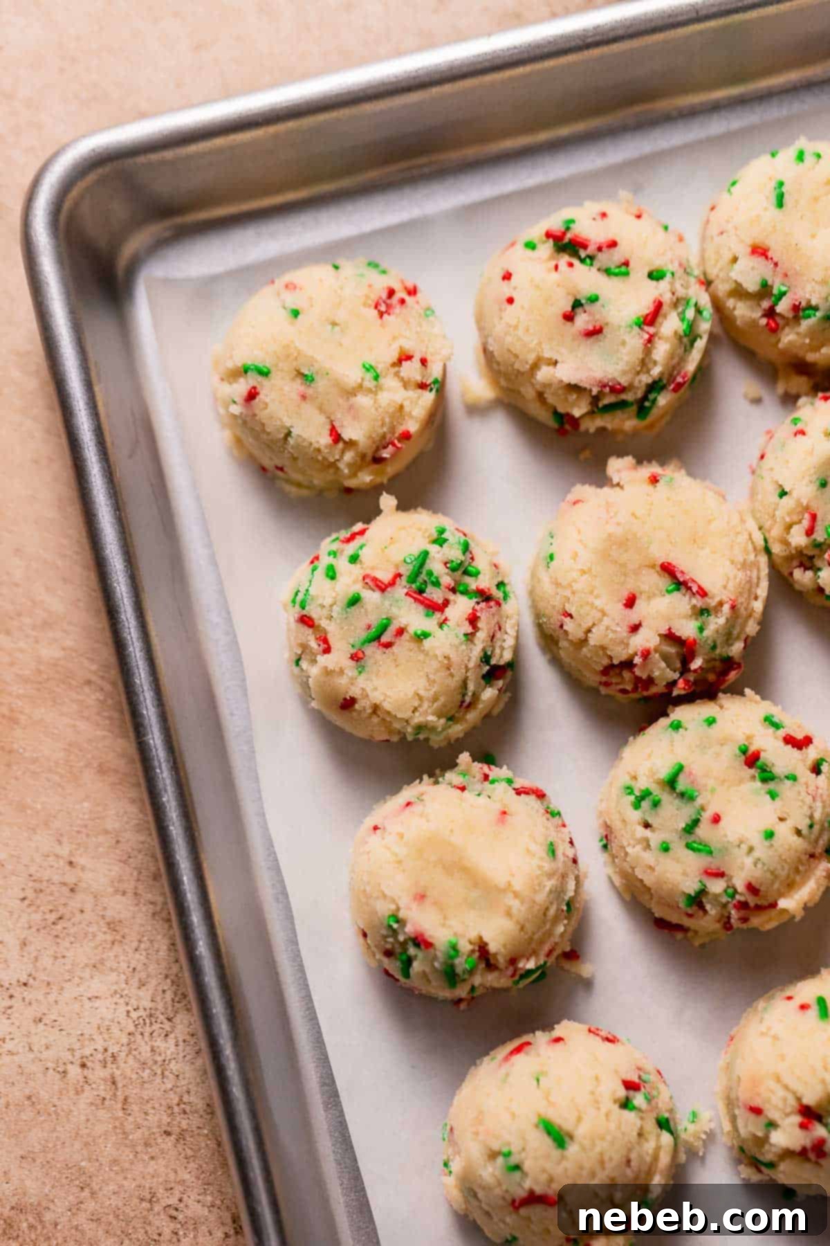 A baking sheet filled with perfectly scooped and flattened sugar cookie dough balls, ready for chilling before being added to the cake.
