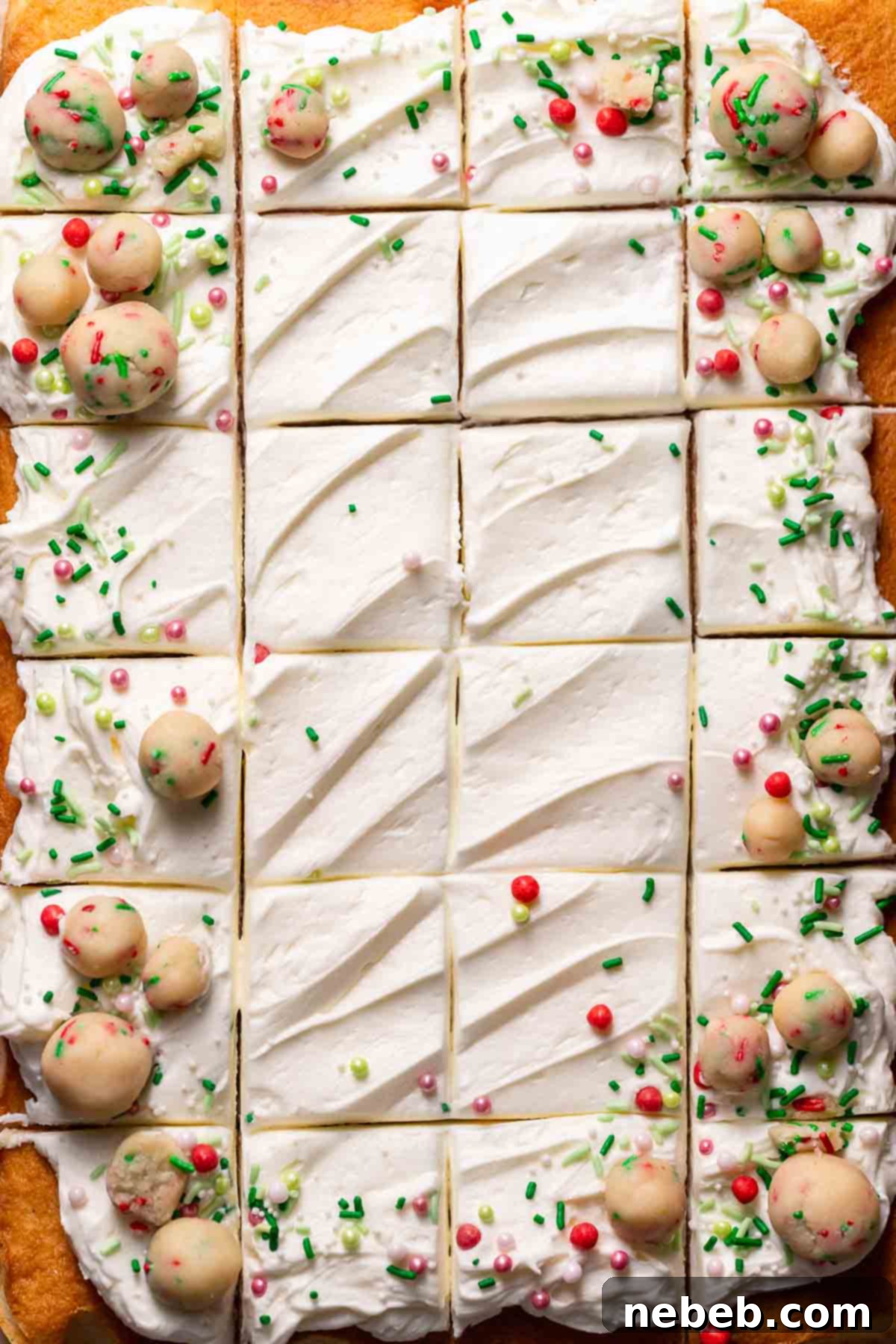 The top of a freshly baked sugar cookie cake, generously decorated with swirls of creamy vanilla frosting, edible sugar cookie dough balls, and a scattering of colorful festive sprinkles.