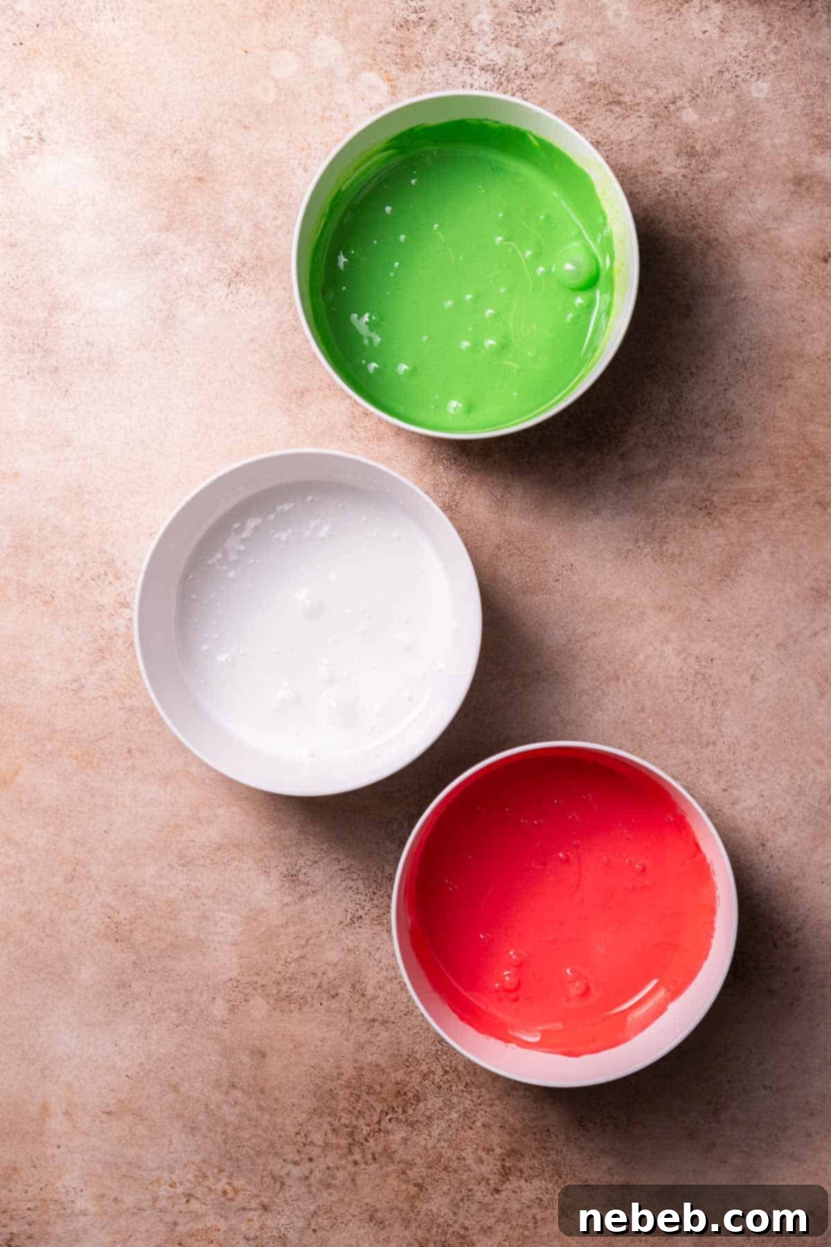 Three bowls of royal icing colored red, white, and green.