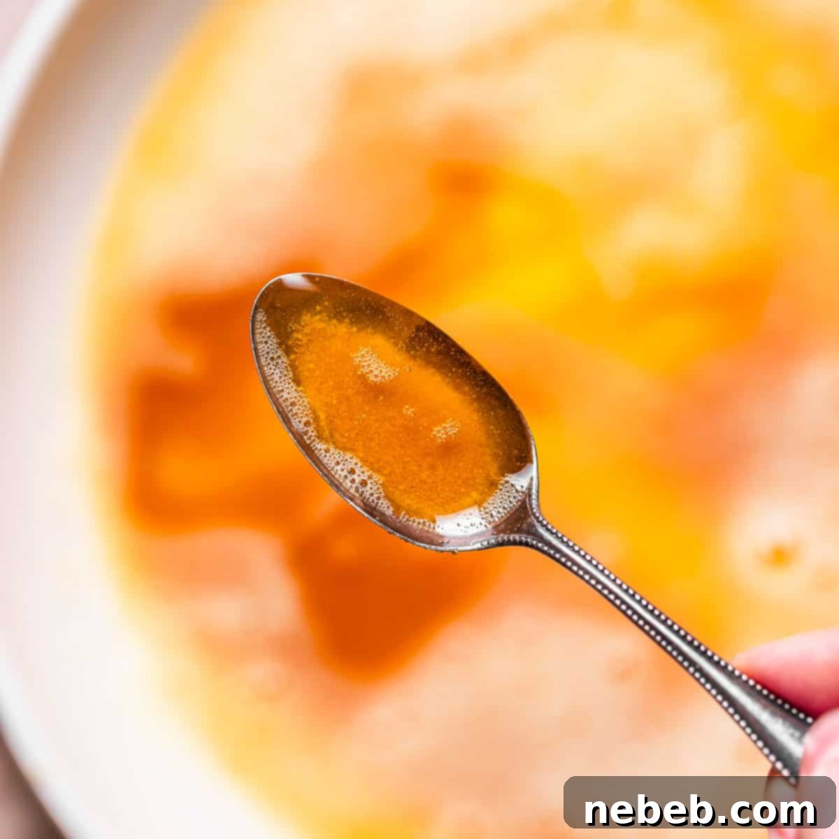 A spoon holding liquid browned butter over a pan, displaying its golden hue and inviting texture.