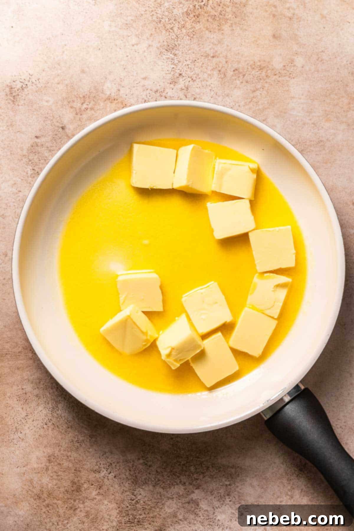 A white pan with butter slices half melted, beginning the browning process.