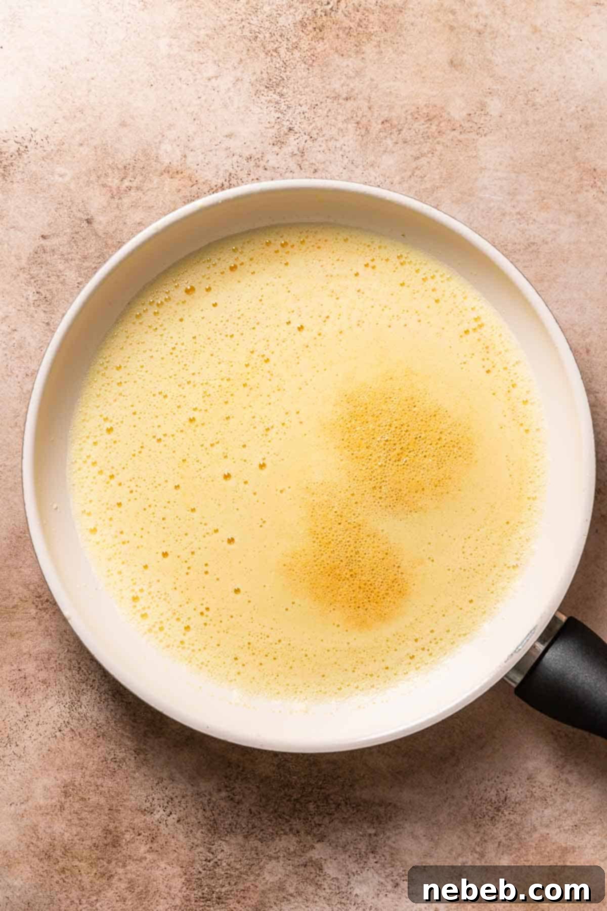 A white pan with melted butter and a thick layer of foam on top, indicating the end of water evaporation.
