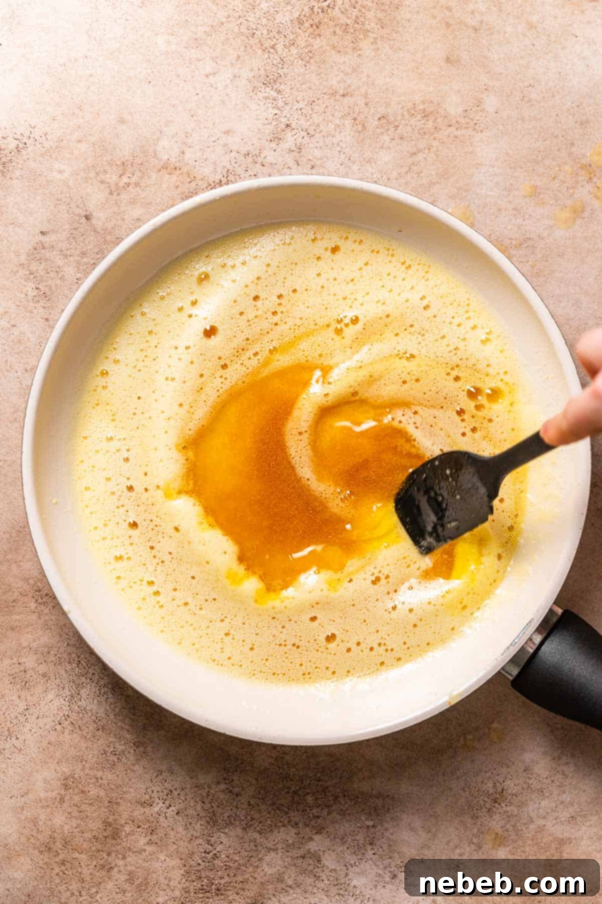 A hand stirring the melted butter in a pan to show the browned milk solids forming at the bottom.
