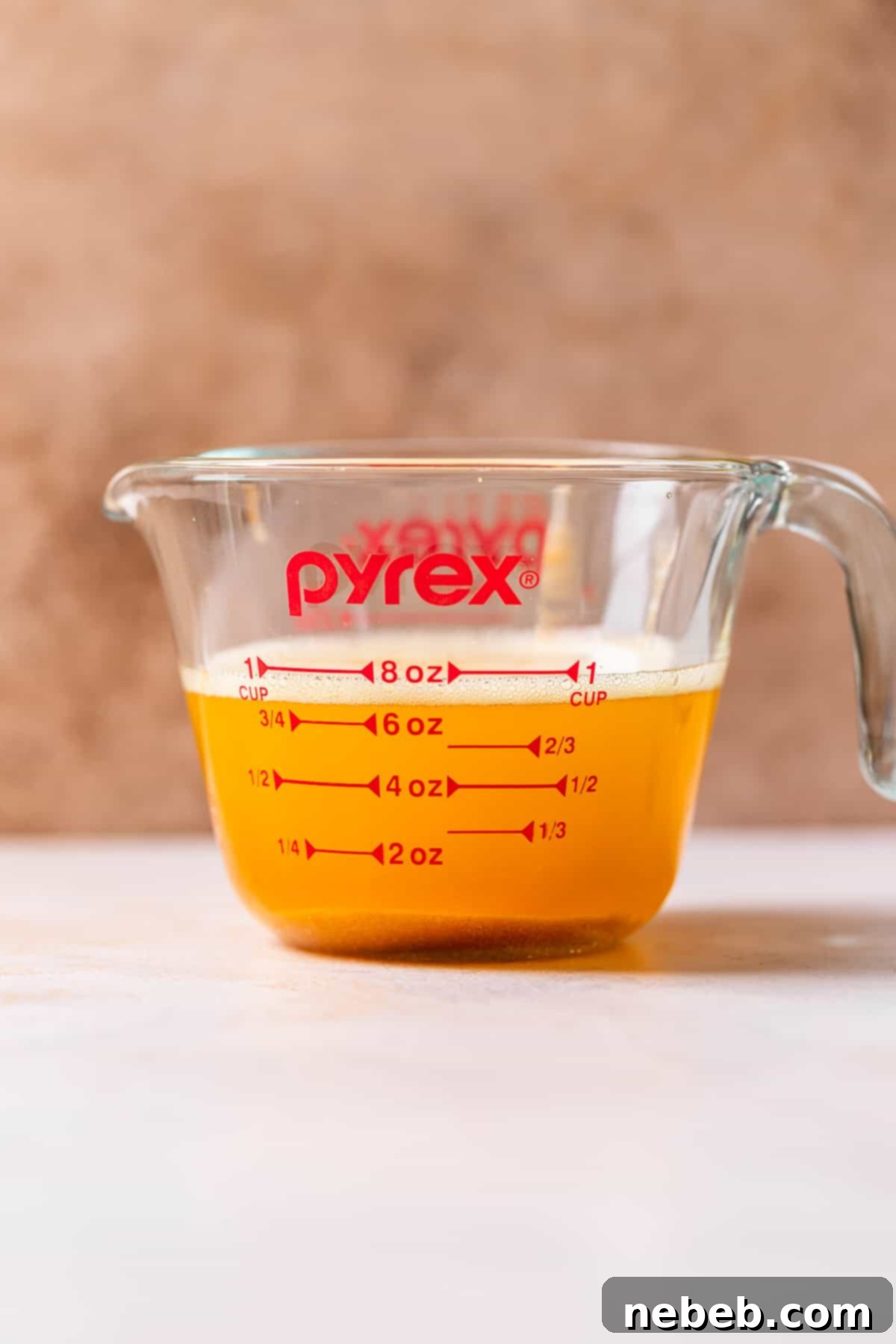 A glass Pyrex measuring cup with browned European butter, illustrating the volume reduction due to moisture loss.
