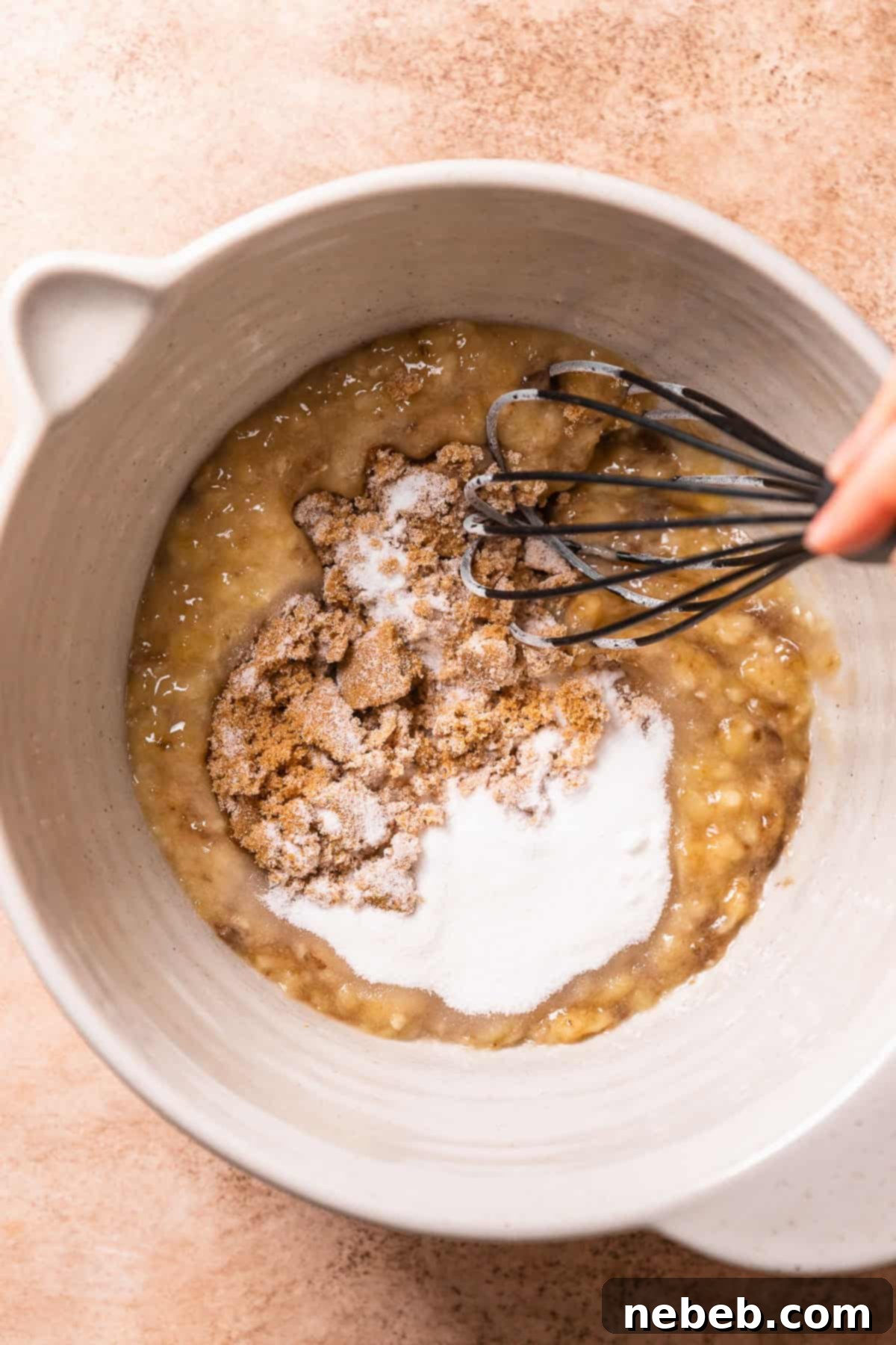 A hand whisking the sugar into the ripe mashed bananas.