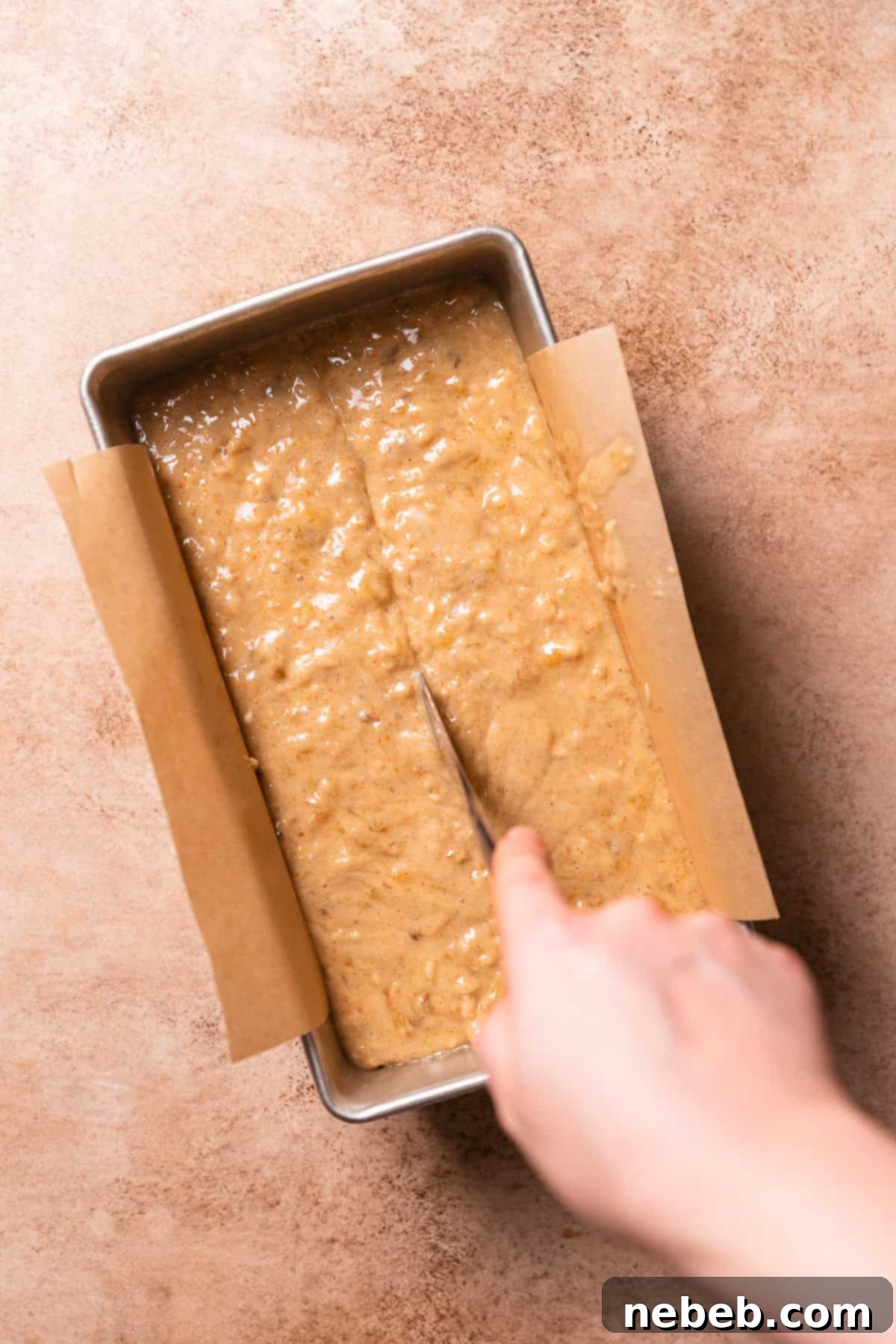 A hand dragging a butter knife through the center of the batter in a loaf pan.