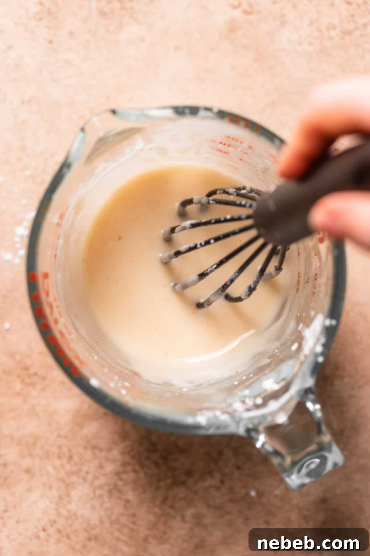 A hand whisking the brown butter glaze in a measuring glass.