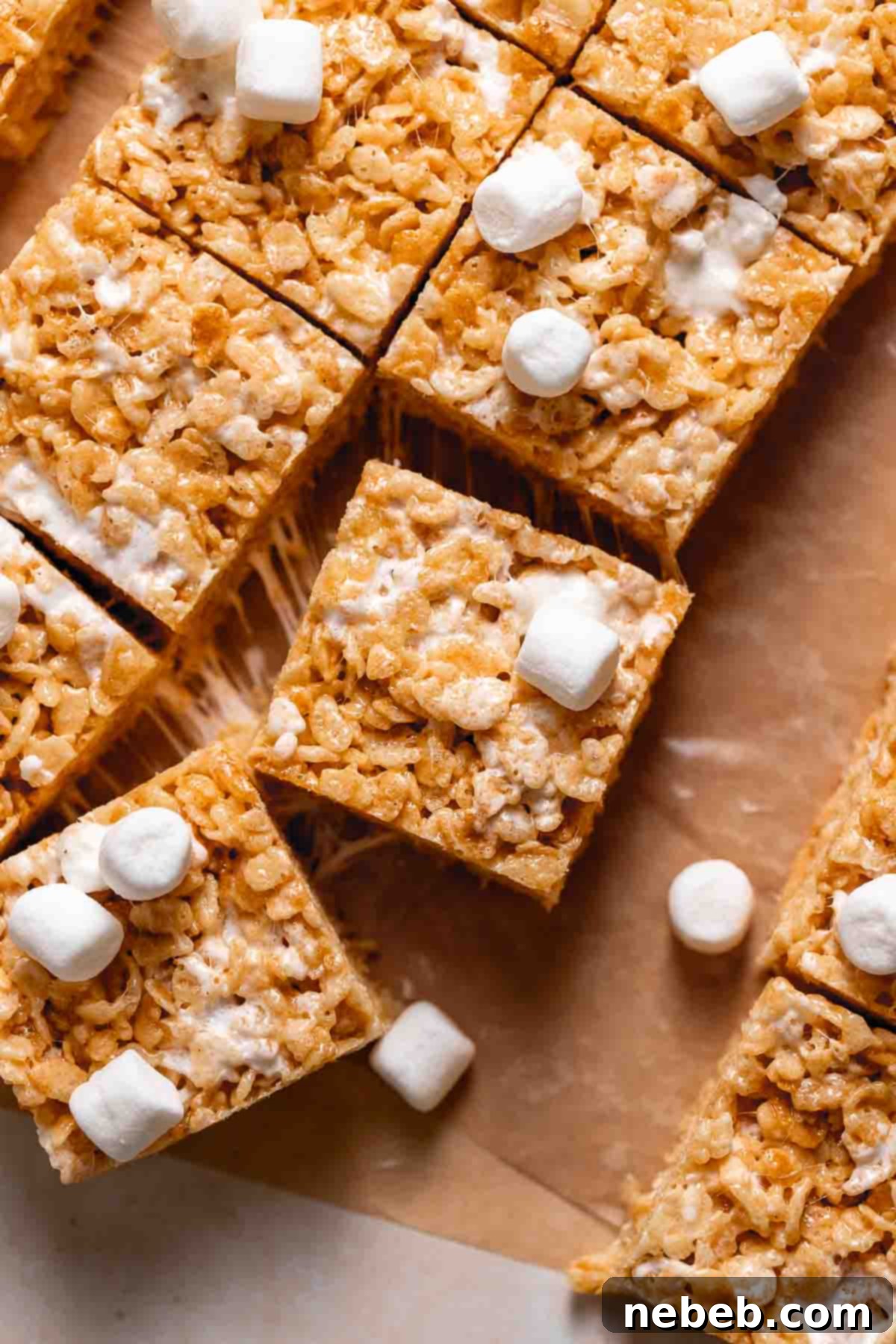 Brown butter rice krispie treats on brown parchment paper with mini marshmallows scattered around.
