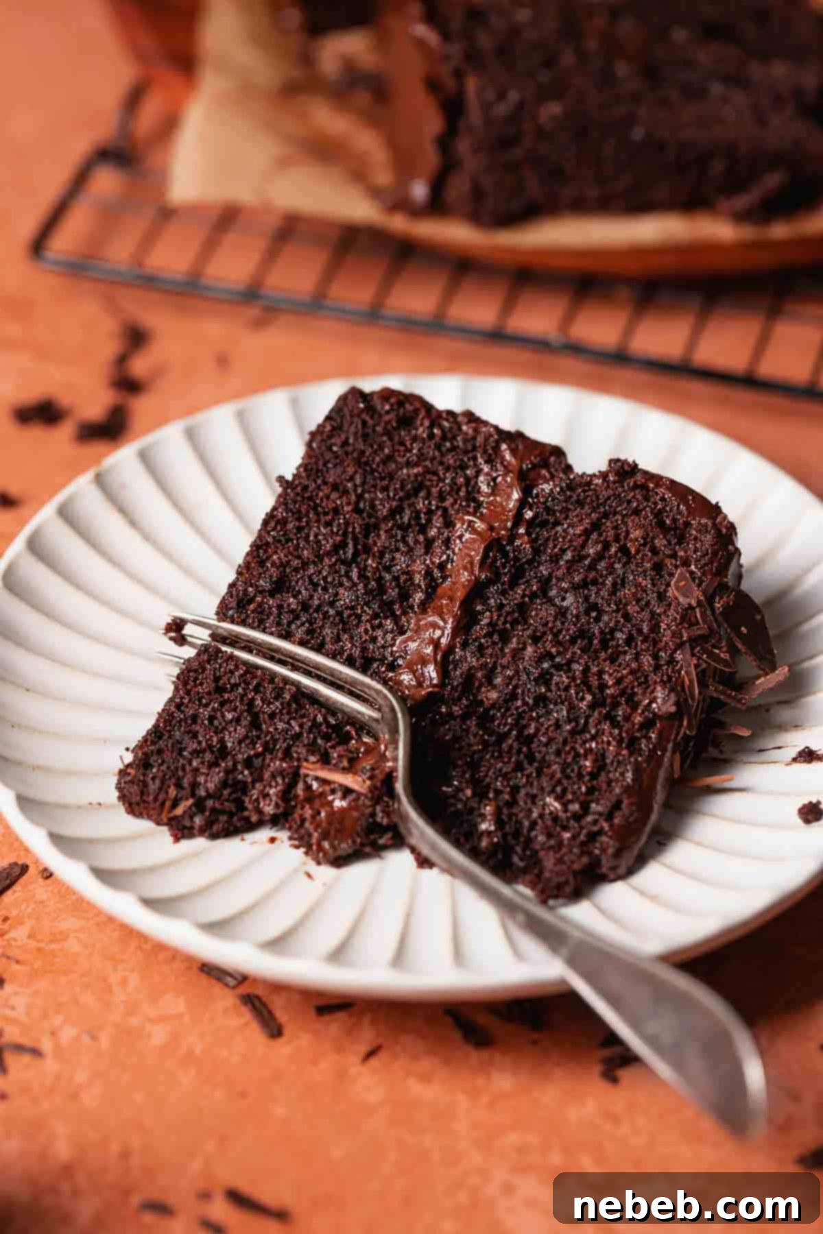 A slice of moist chocolate cake with chocolate frosting on a white plate with a fork digging into it.