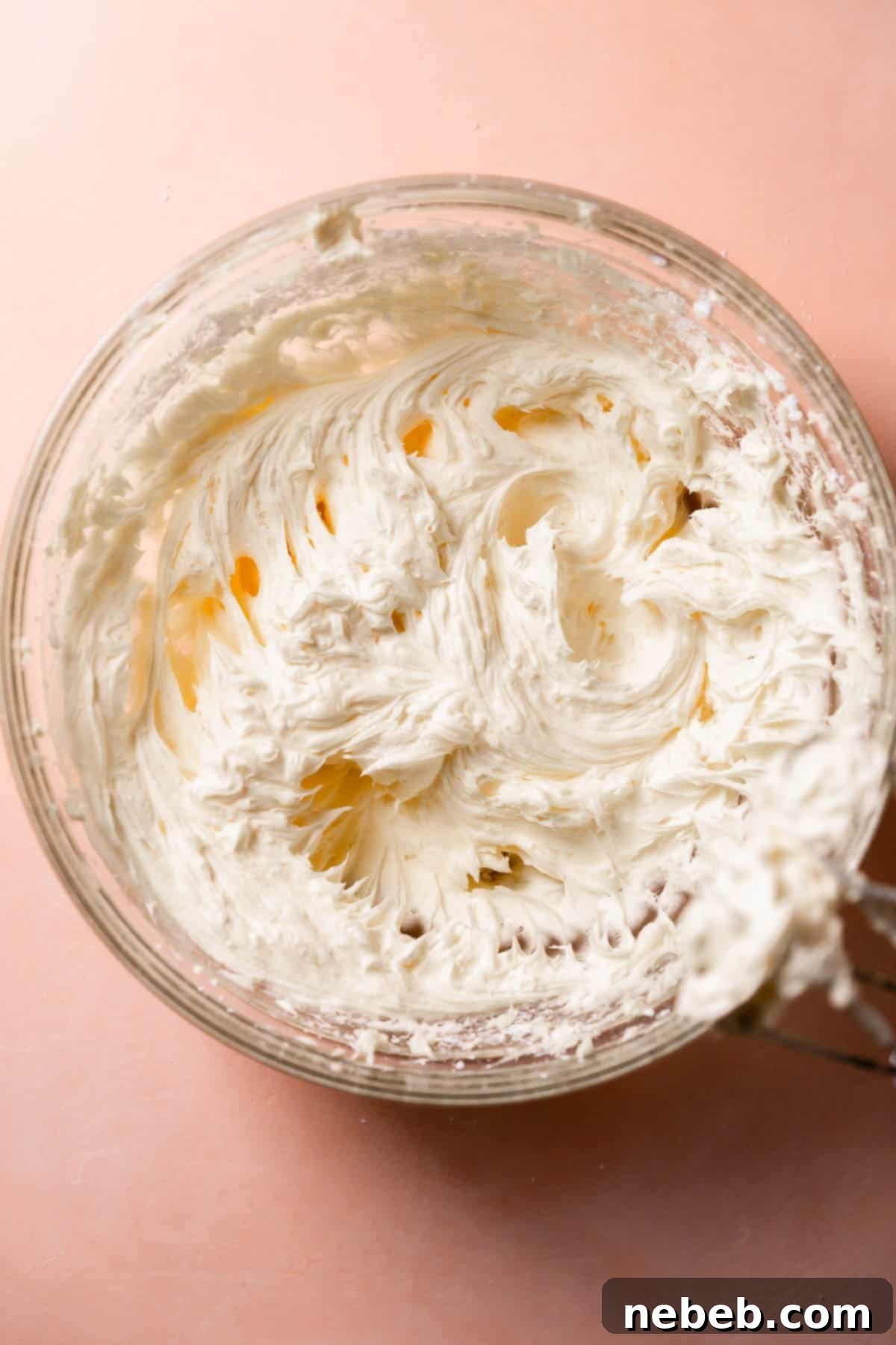 A glass mixing bowl with the cream cheese buttercream after mixing in the powdered sugar.