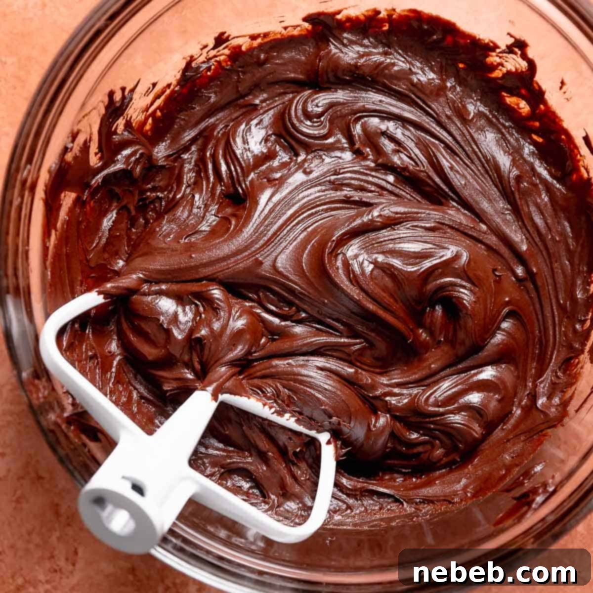 A bowl of chocolate fudge frosting with a white paddle attachment.