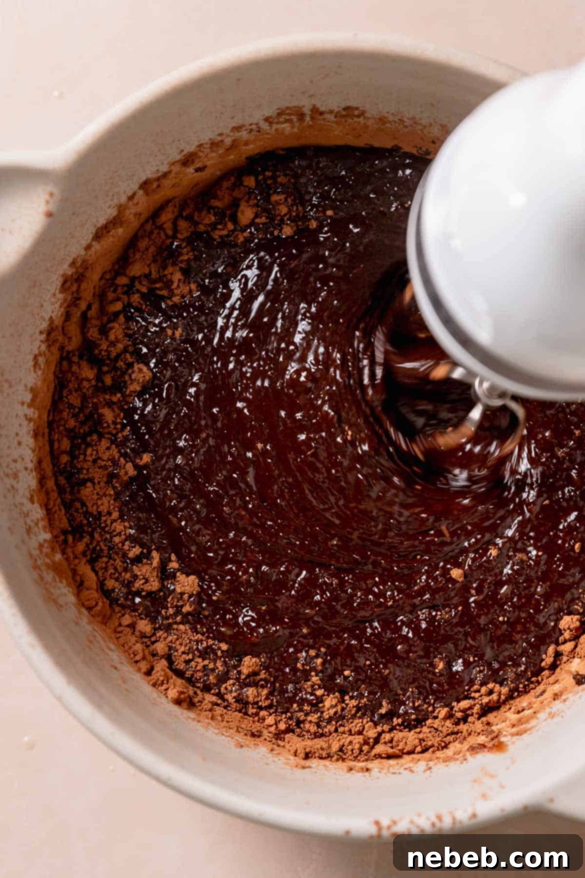 A hand mixer beating the melted chocolate mixture into the cocoa powder.