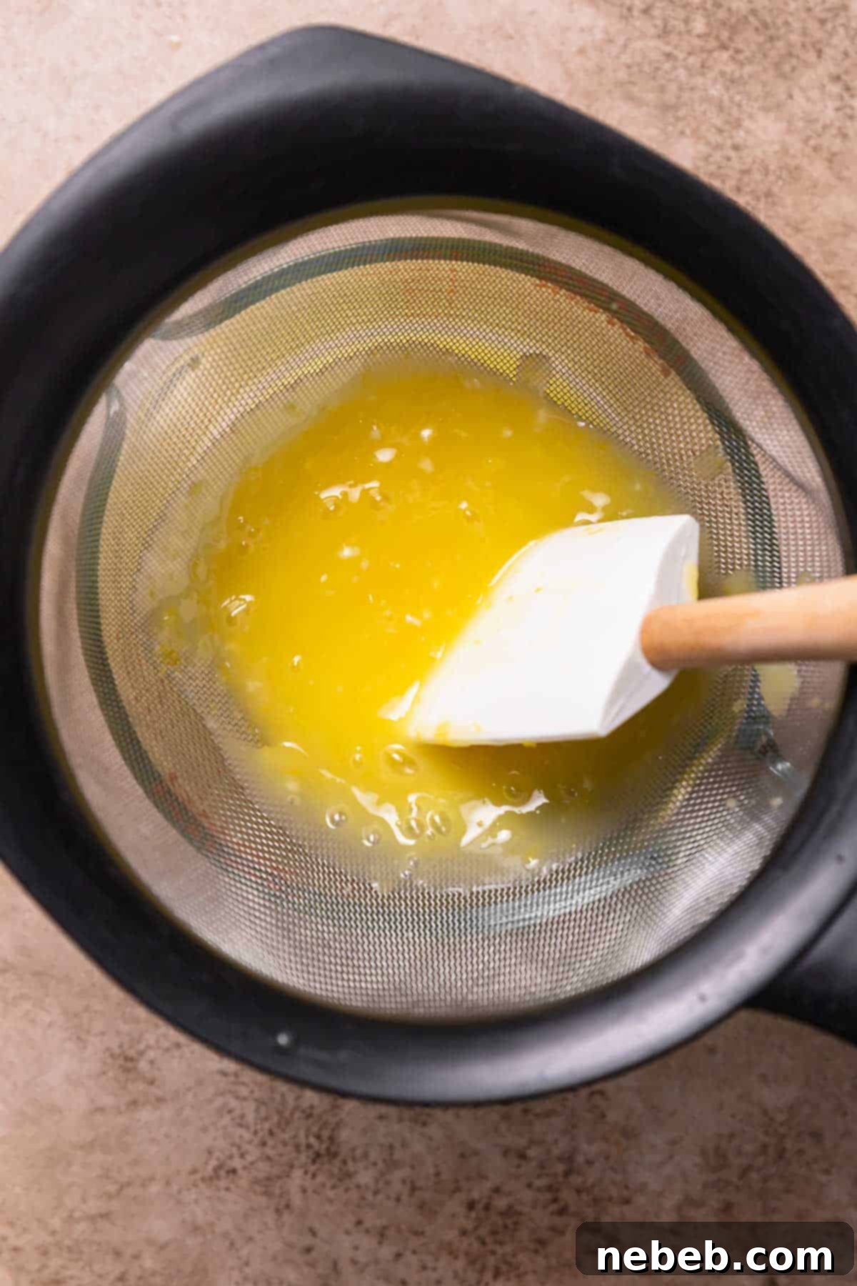 Thickened lemon curd being pressed through a fine mesh strainer into a clean bowl, ensuring a perfectly smooth texture.