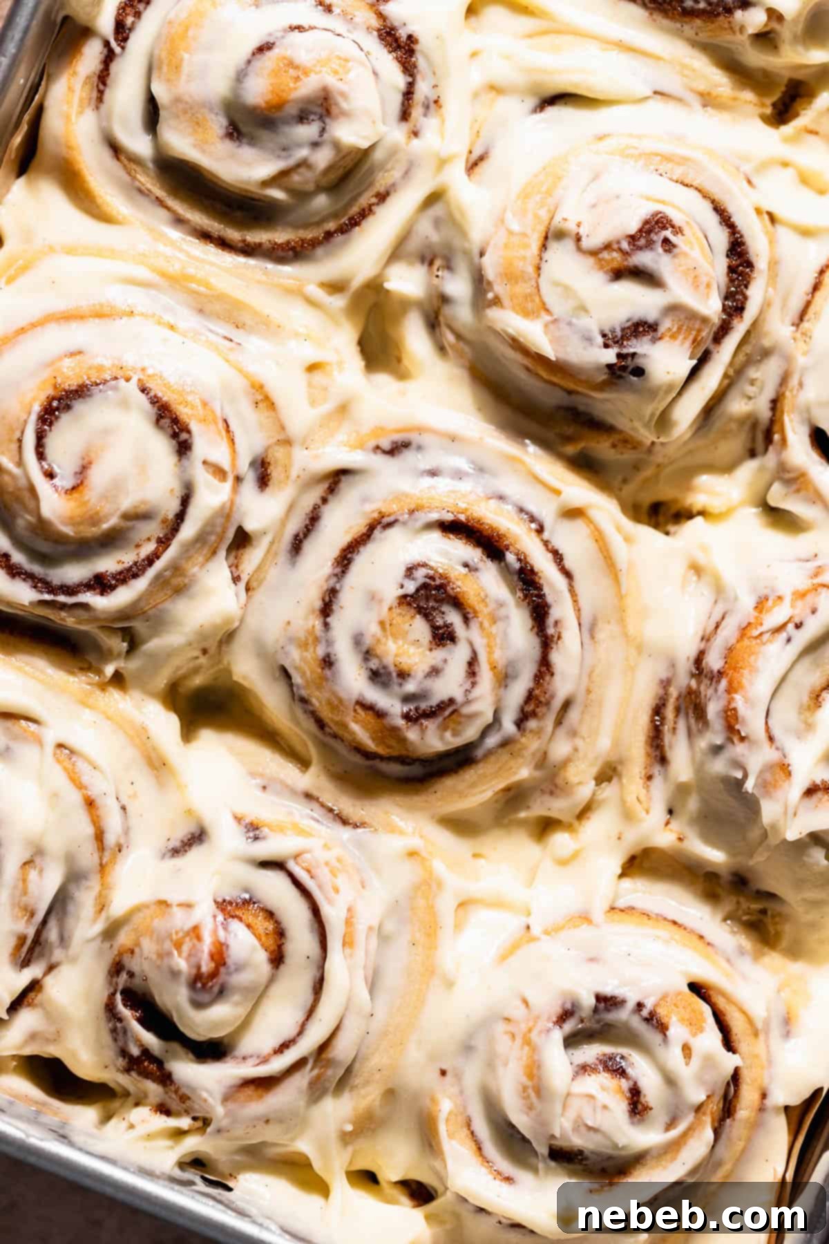 Cinnamon rolls generously topped with cream cheese frosting in a baking pan.