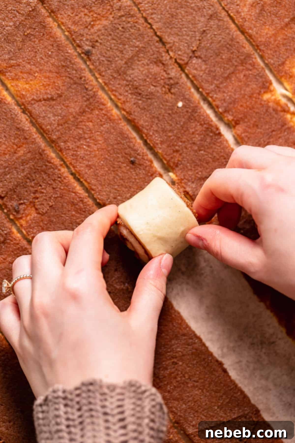 Two hands rolling up the cinnamon dough into a tight log, ready to be cut into rolls.