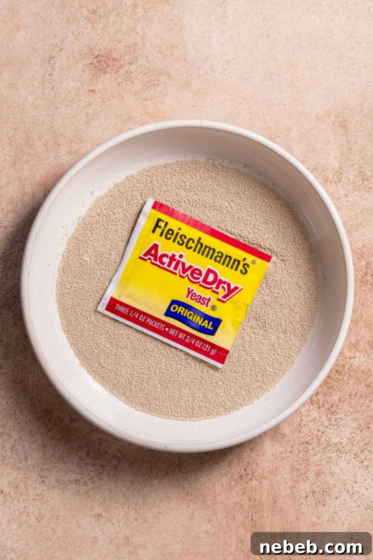 A white bowl full of yeast and a packed of unopened yeast, ready for baking.