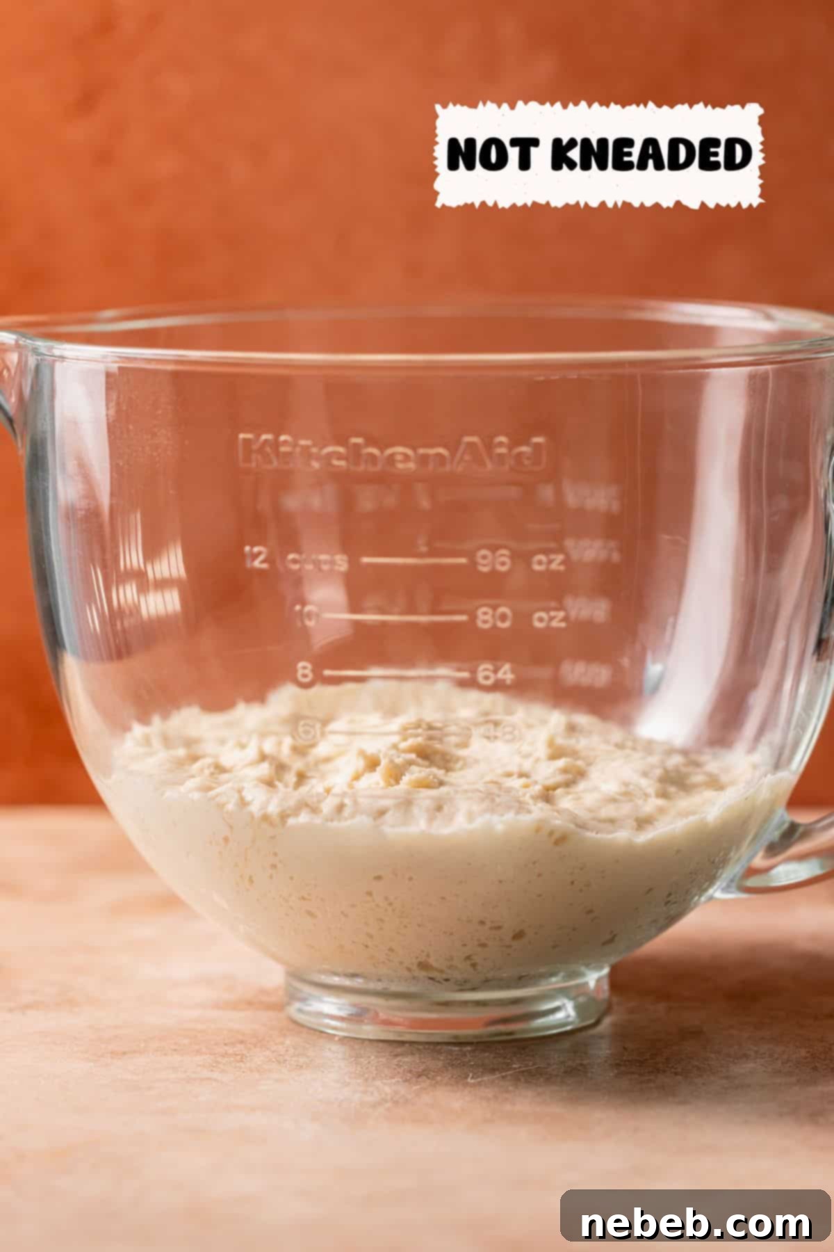 A glass mixing bowl with dough that hasn't been kneaded, showing minimal volume after rising.